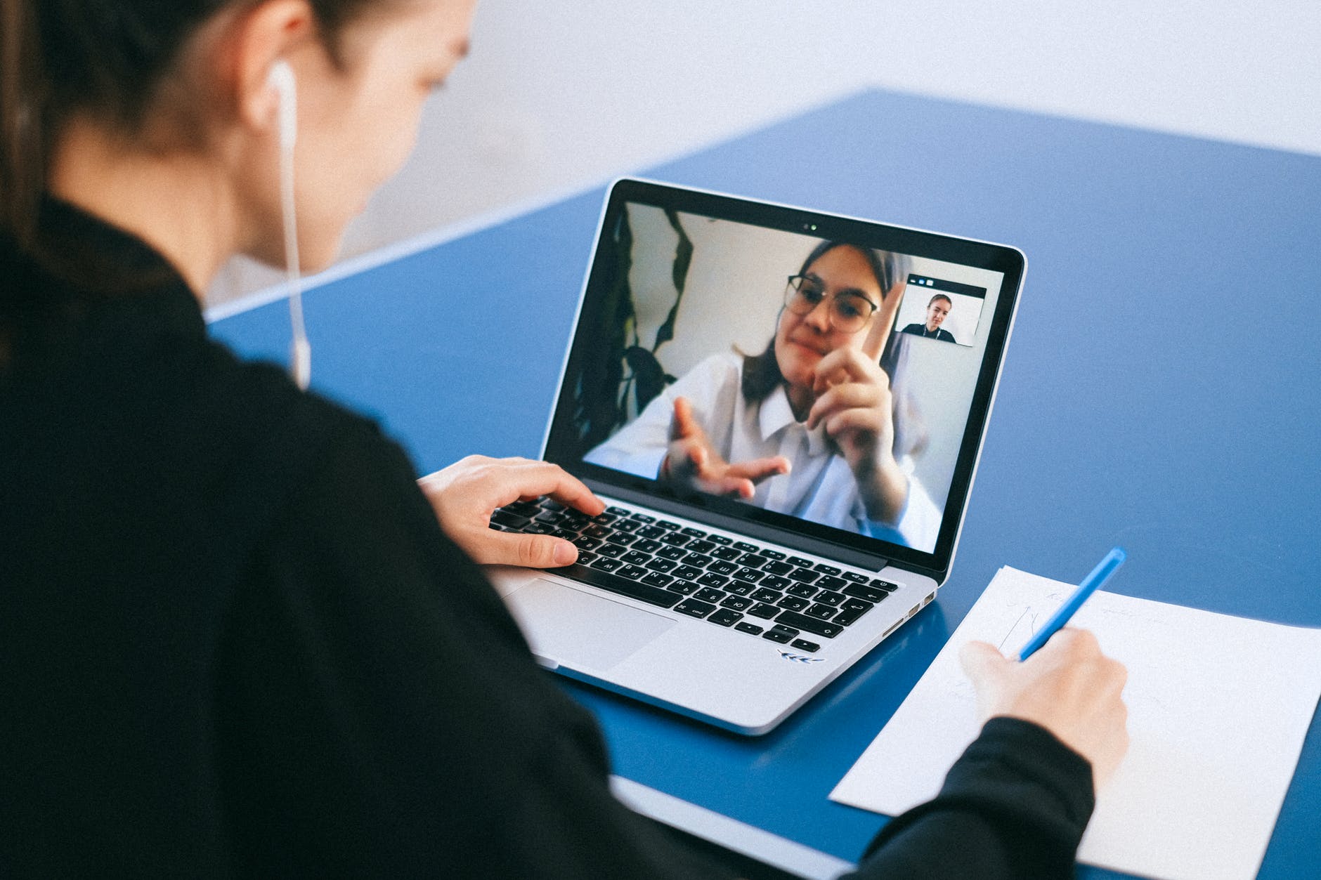 Woman working on laptop wearing earbuds. Laptop screen shows another woman in video conference.