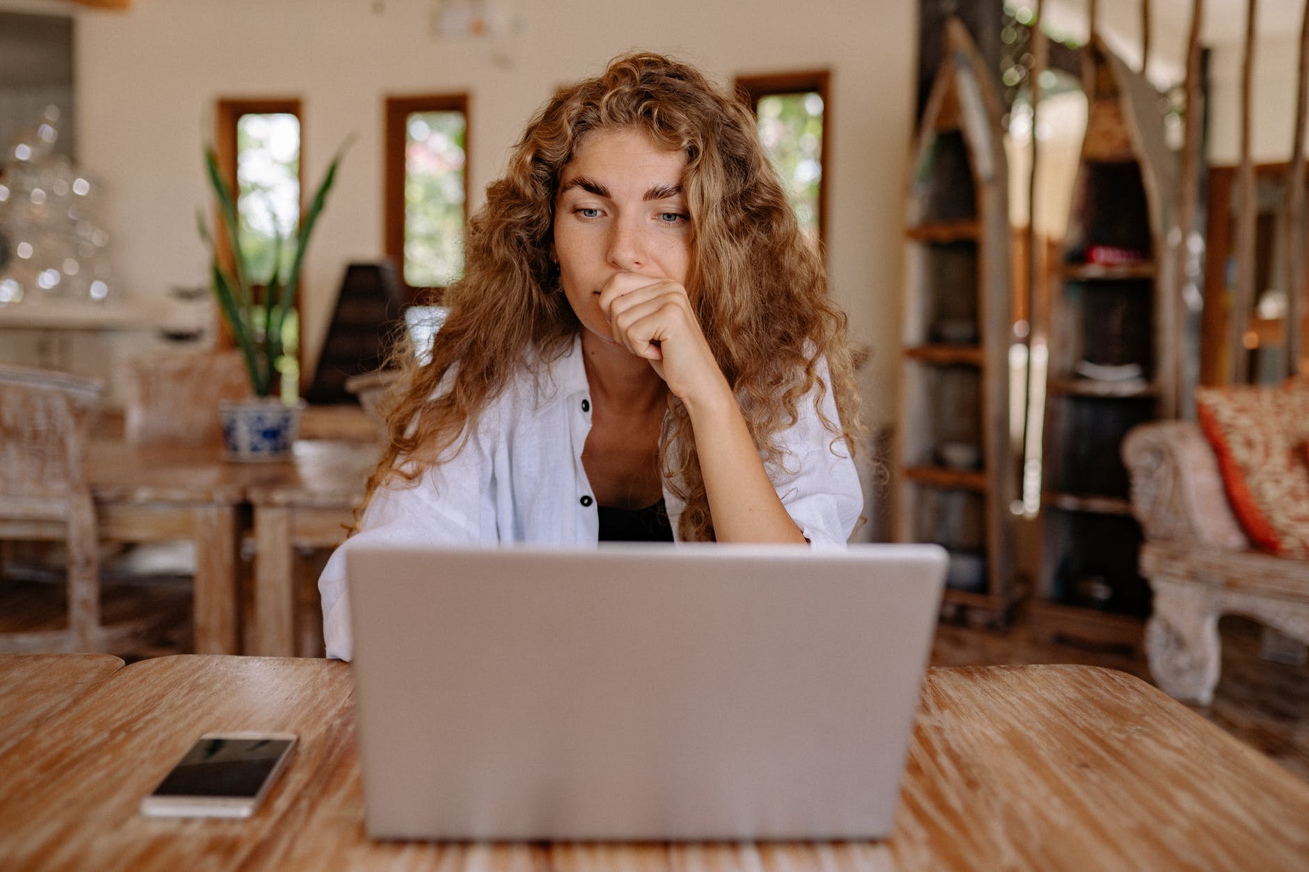 Woman with curly brown hair working on laptop at table.