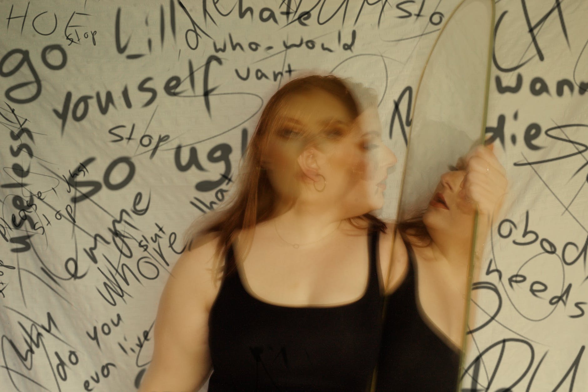 Blurred photo of woman wearing black tank top. Behind woman black text on white background.