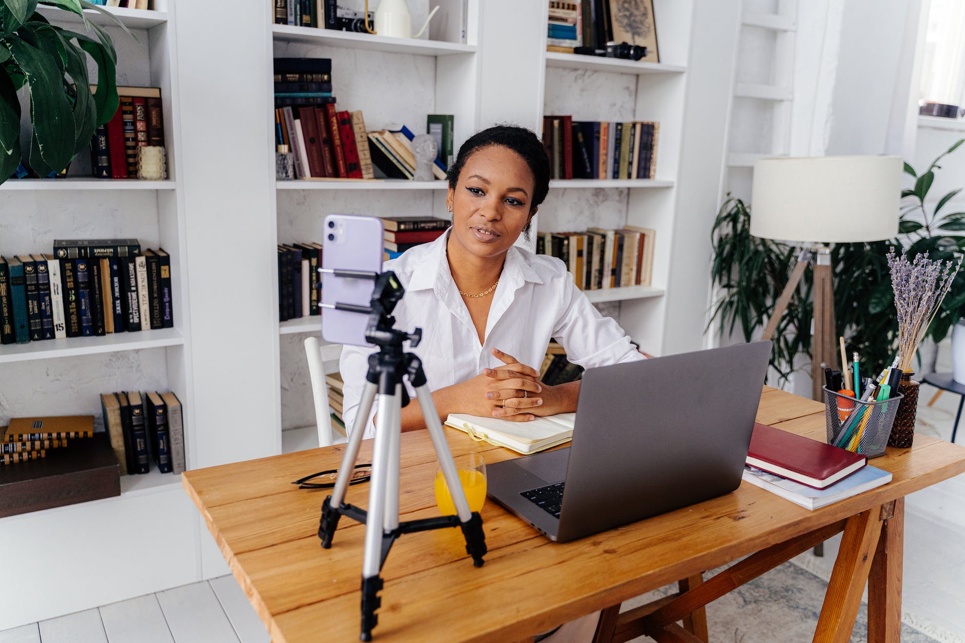 Black woman at desk with open laptop, notebooks, and a phone on a tripod.