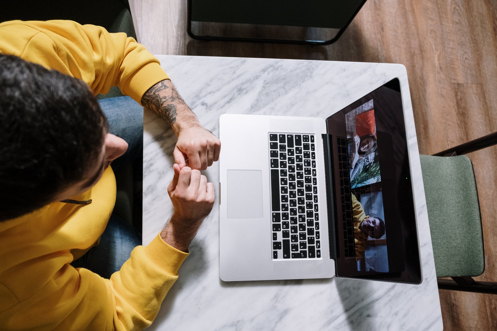 Top view of person wearing mustard yellow sweatshirt and using hands to sign in front of laptop with video conferencing.