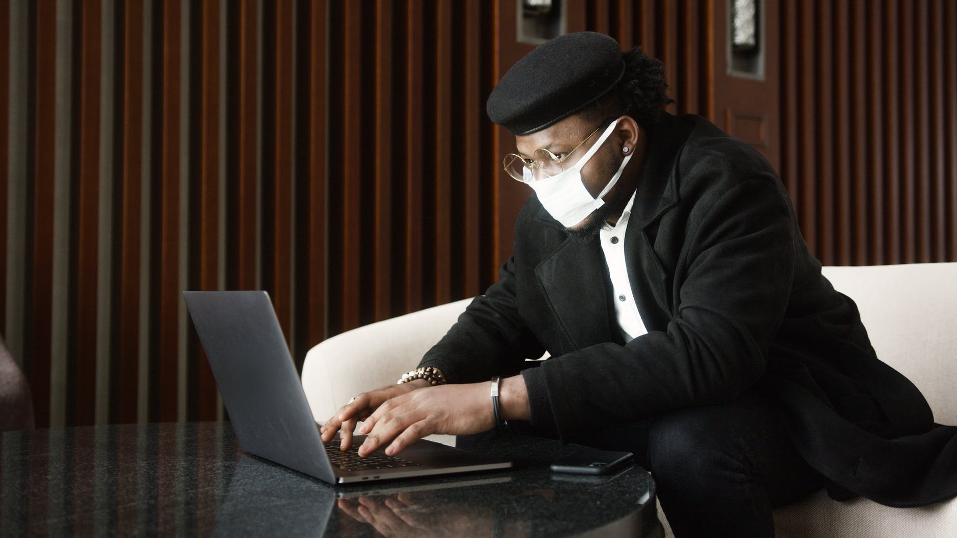 Black man wearing black cap and typing on laptop.