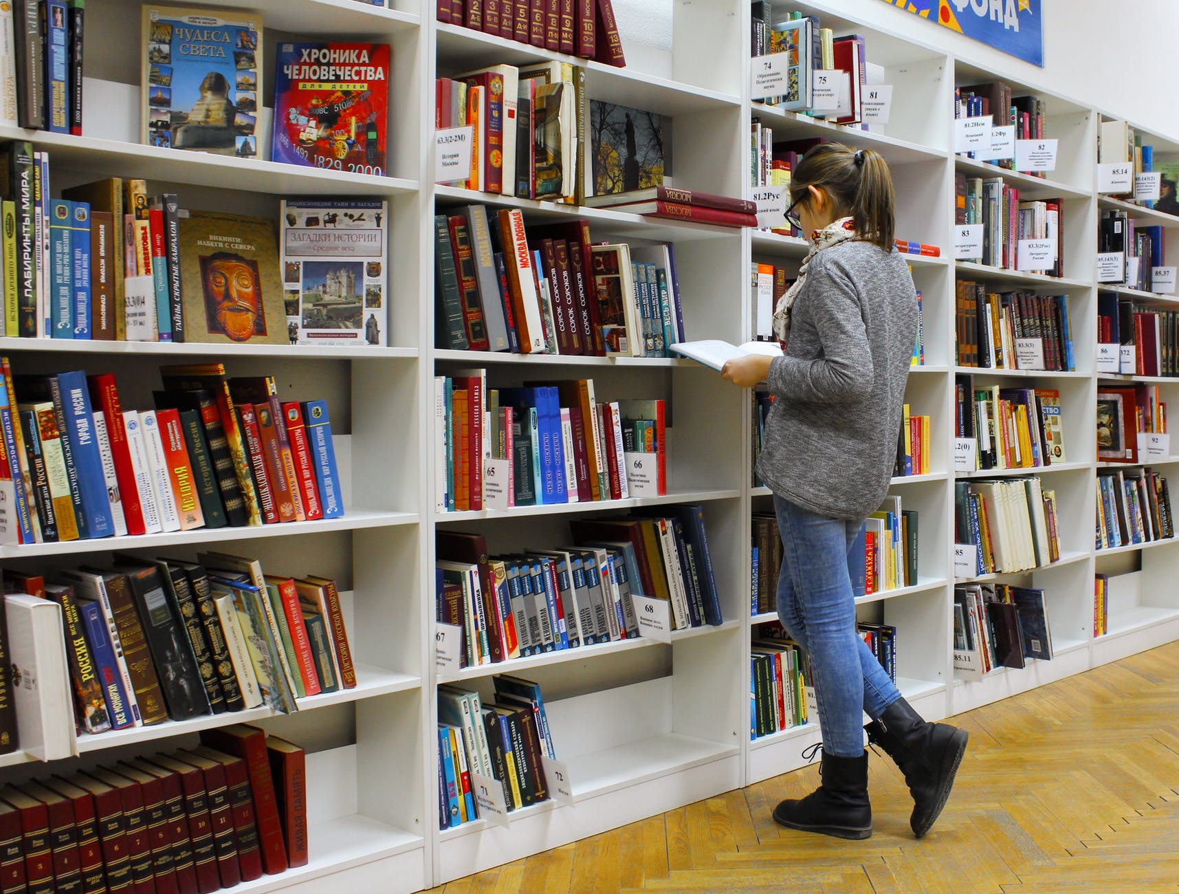 Woman reading book in front of large book cases.