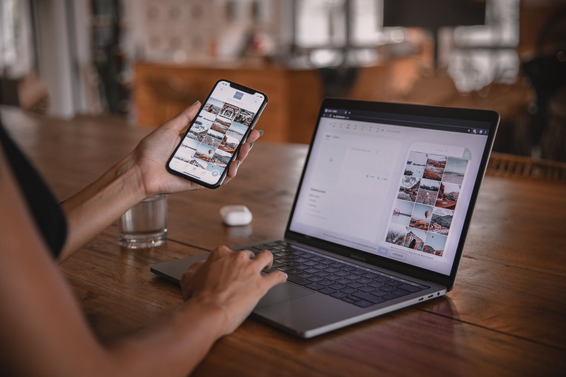 Hand holding smart phone with images on the screen and typing on laptop.