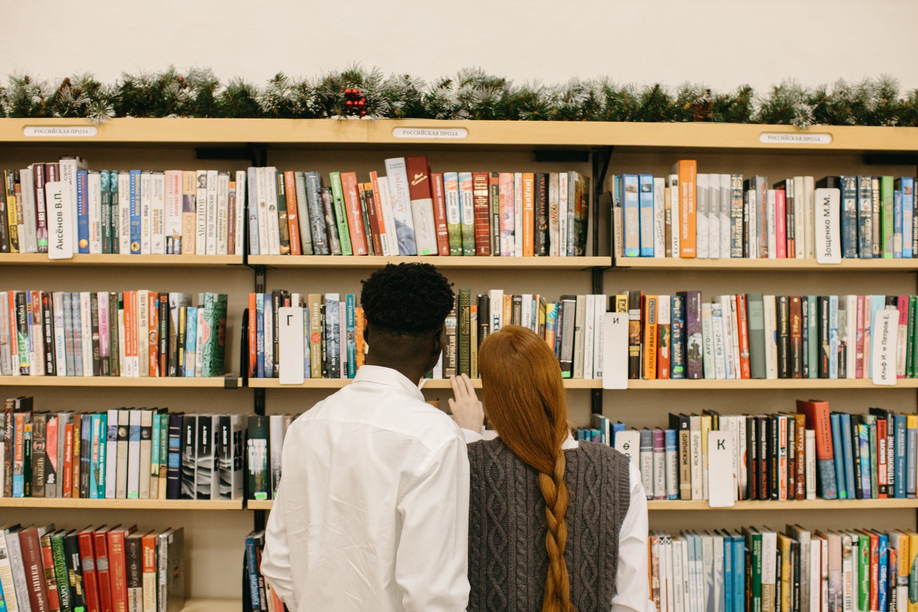 Black man and red hair woman facing large bookcase full of books.