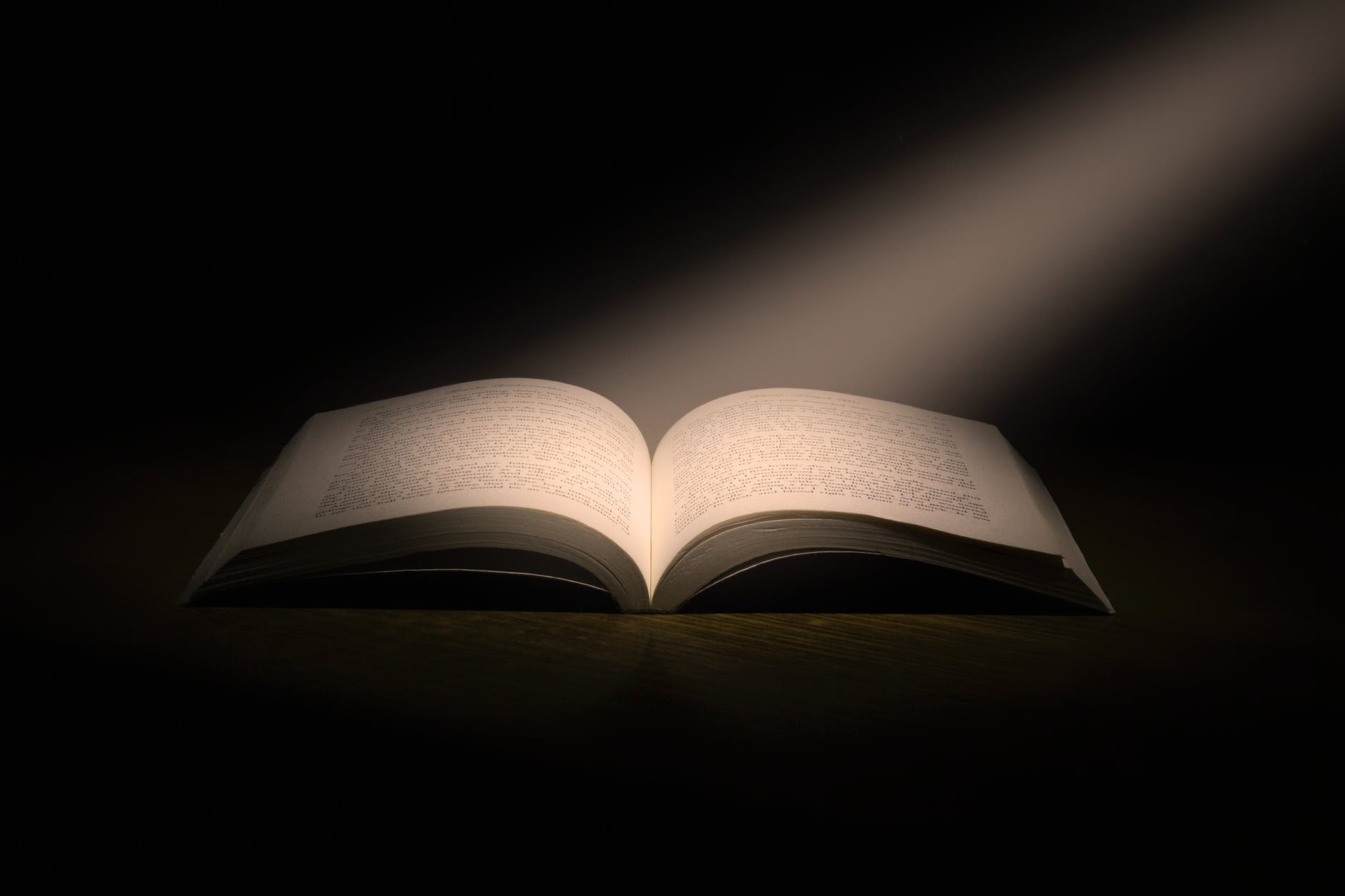 Open book in dark room with light reflecting on open pages.
