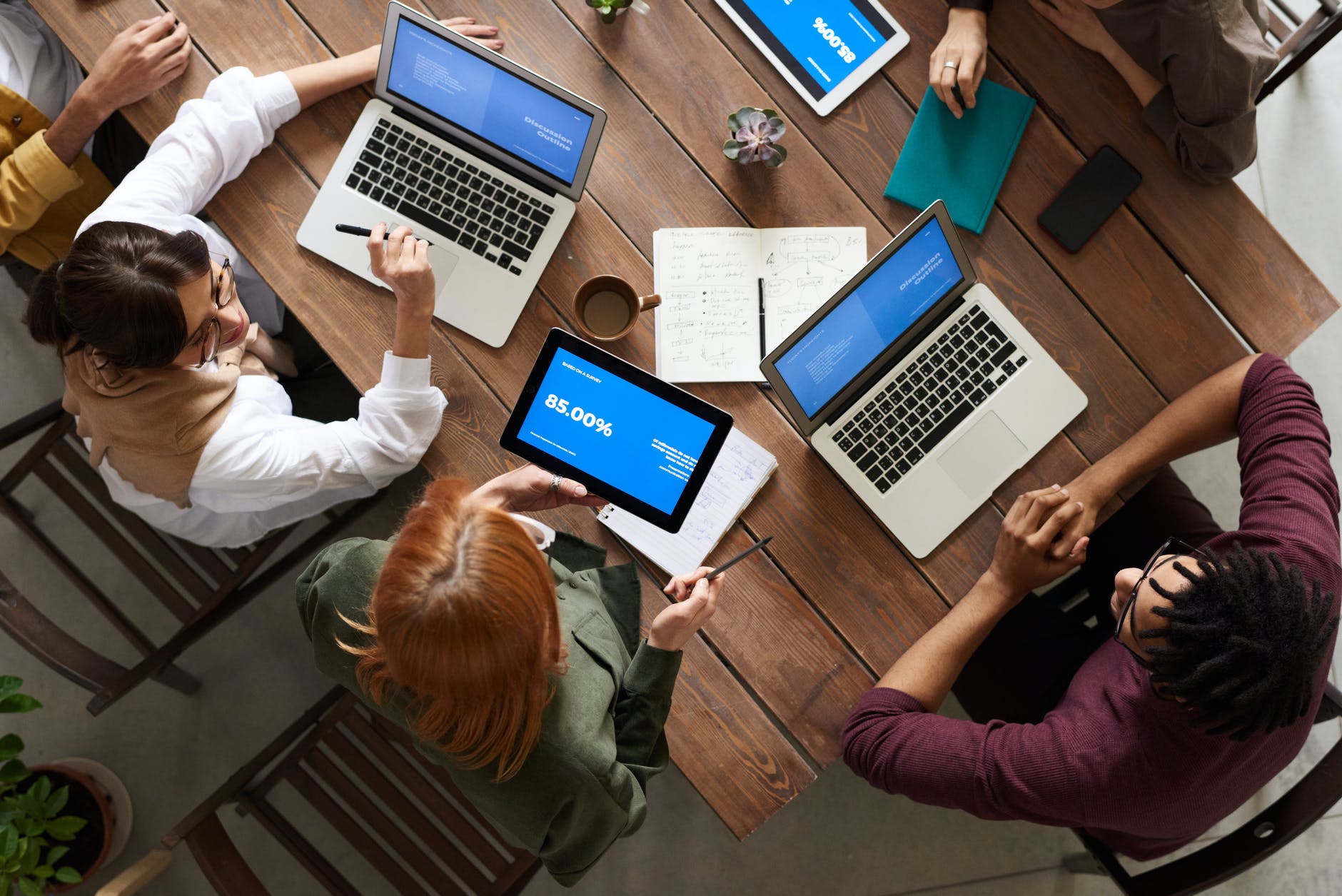Top down view of table with several laptops and people working together.