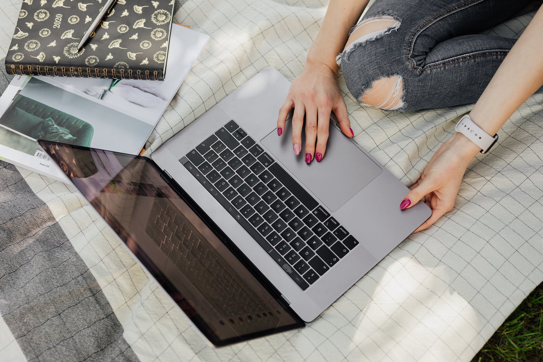 Top view of open laptop and hands with purple nails on trackpad.