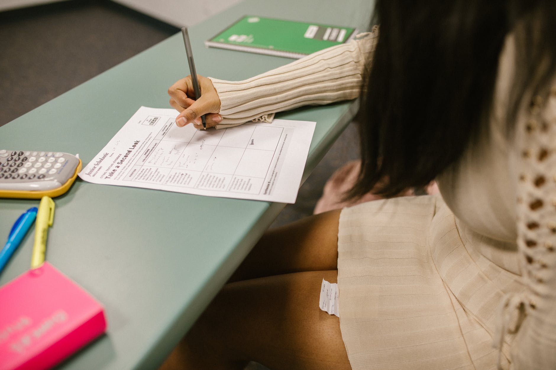 Student working on worksheet at desk and has paper note under desk.