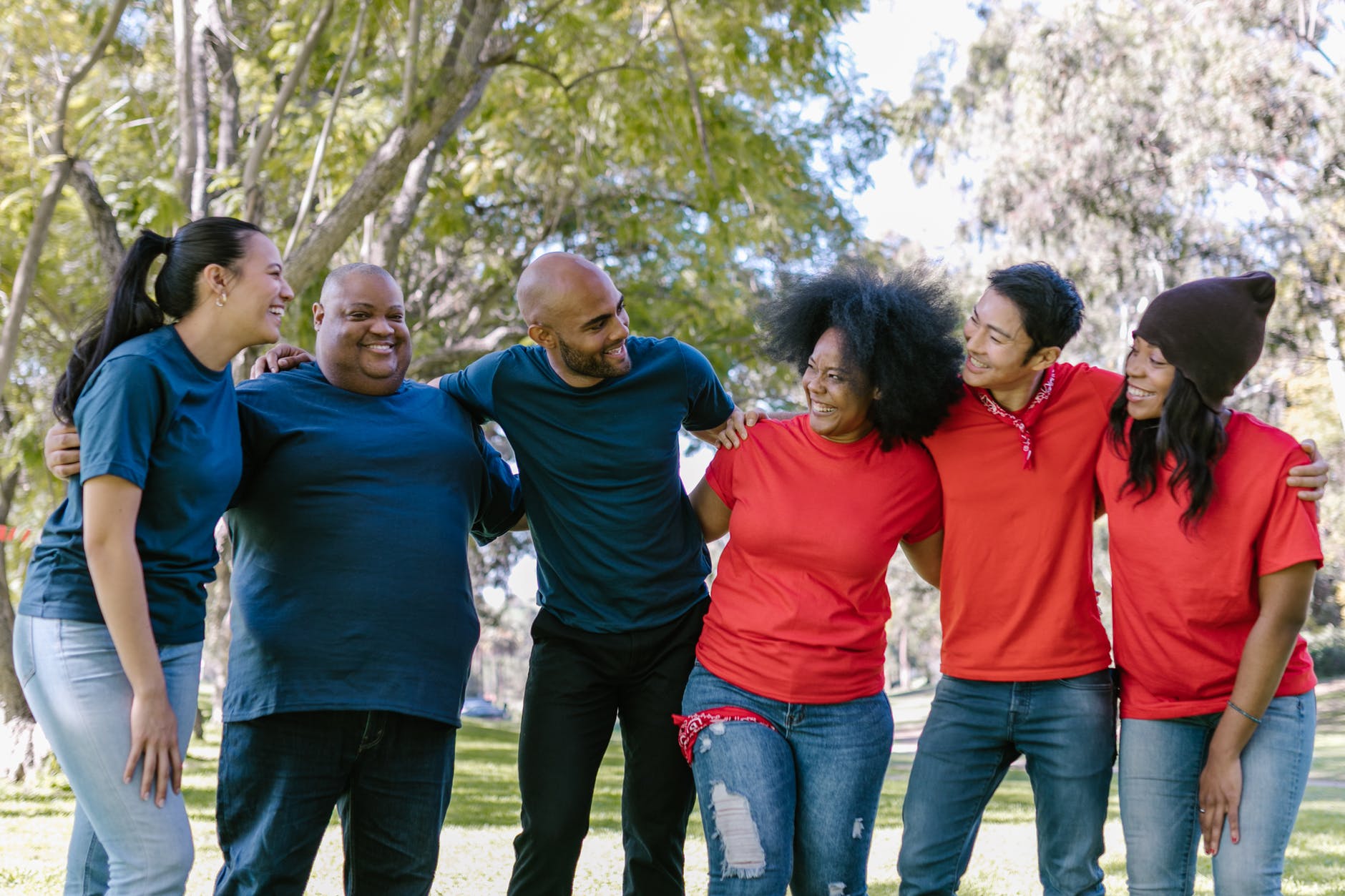 Six people standing outside shoulder to shoulder. Three are wearing blue shirts on the left, and three are wearing red shirts on the right.
