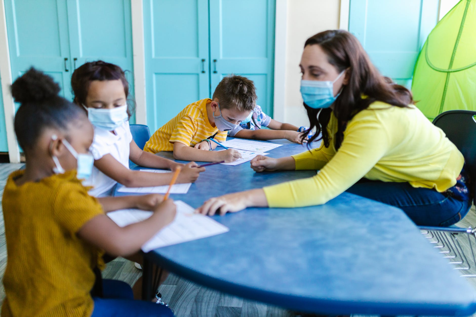 Teacher wearing mask working with several grade school students around a table.
