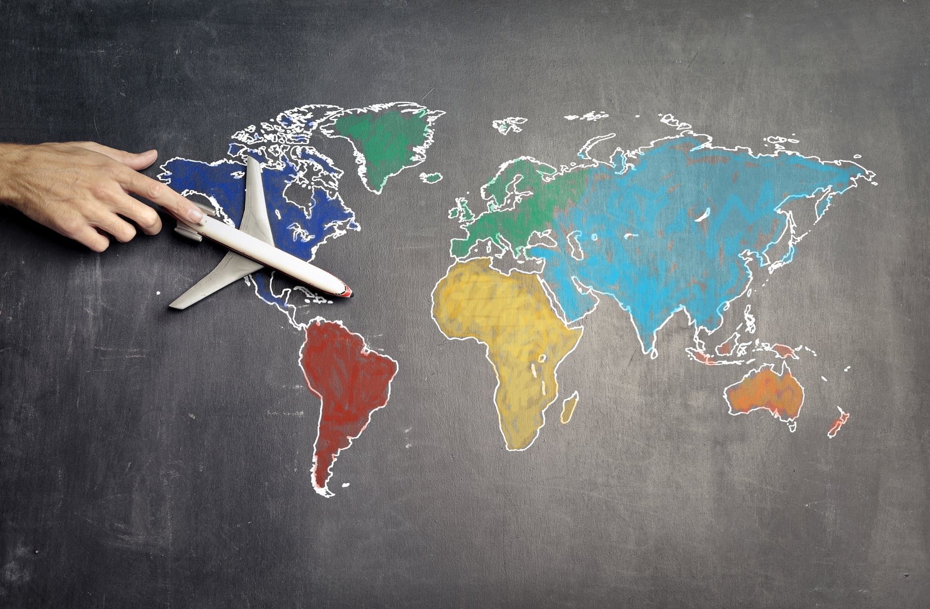 World map on chalkboard
Continents are in different colors
Airplane model held by hand is over North America