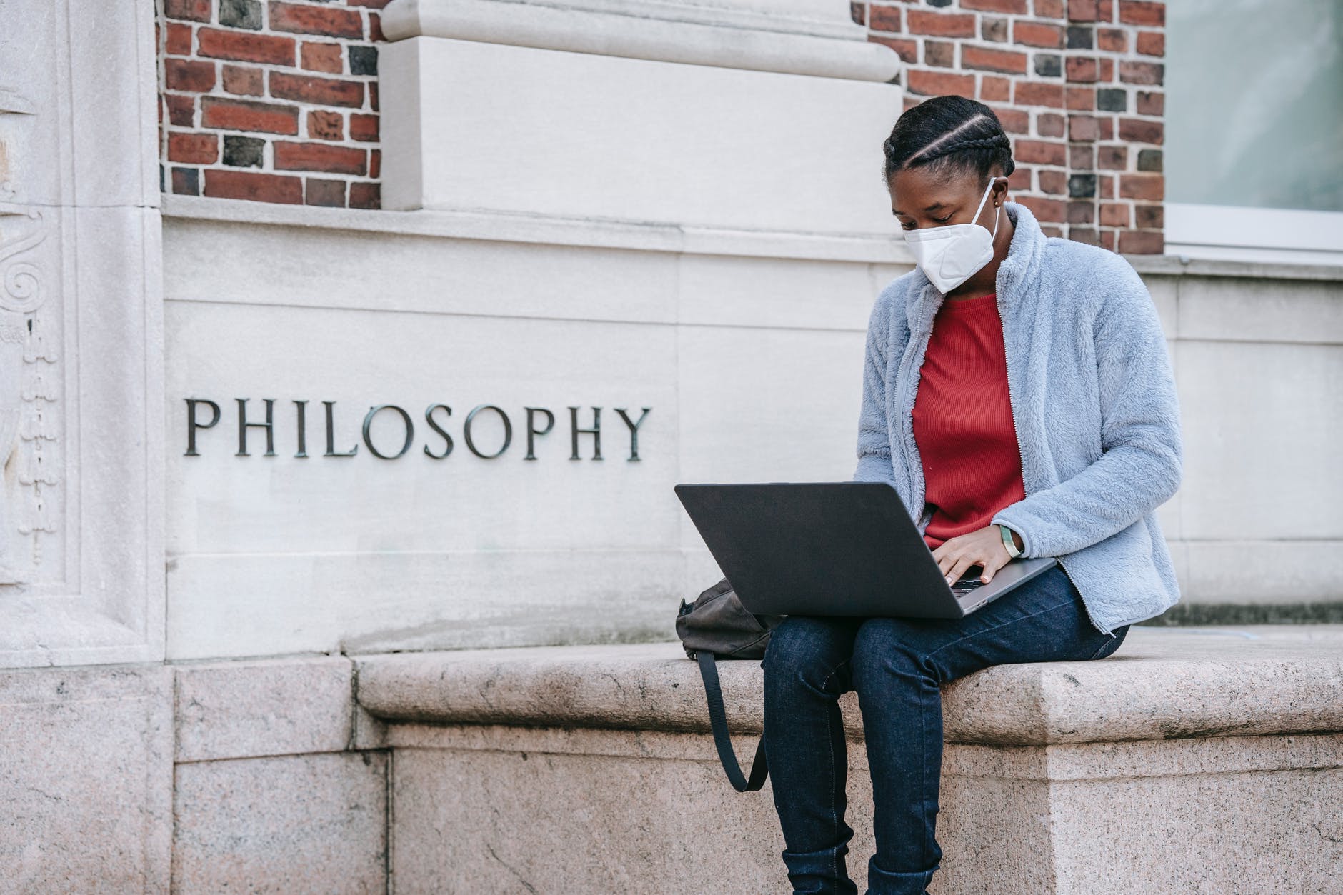 Black woman wearing mask and working on computer while seated outside Philosophy building