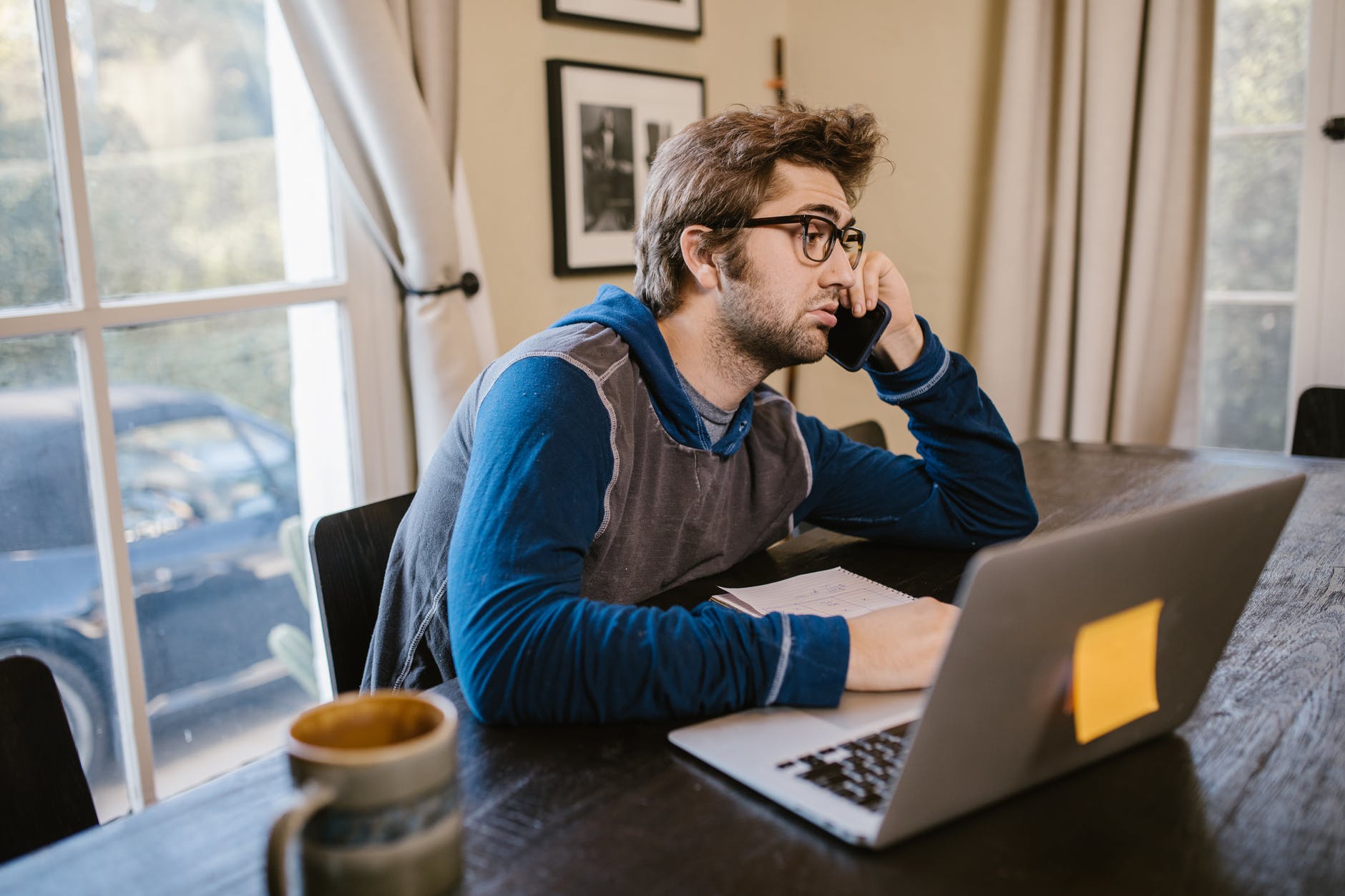 Man with glasses and brown hair on phone and in front of open laptop.