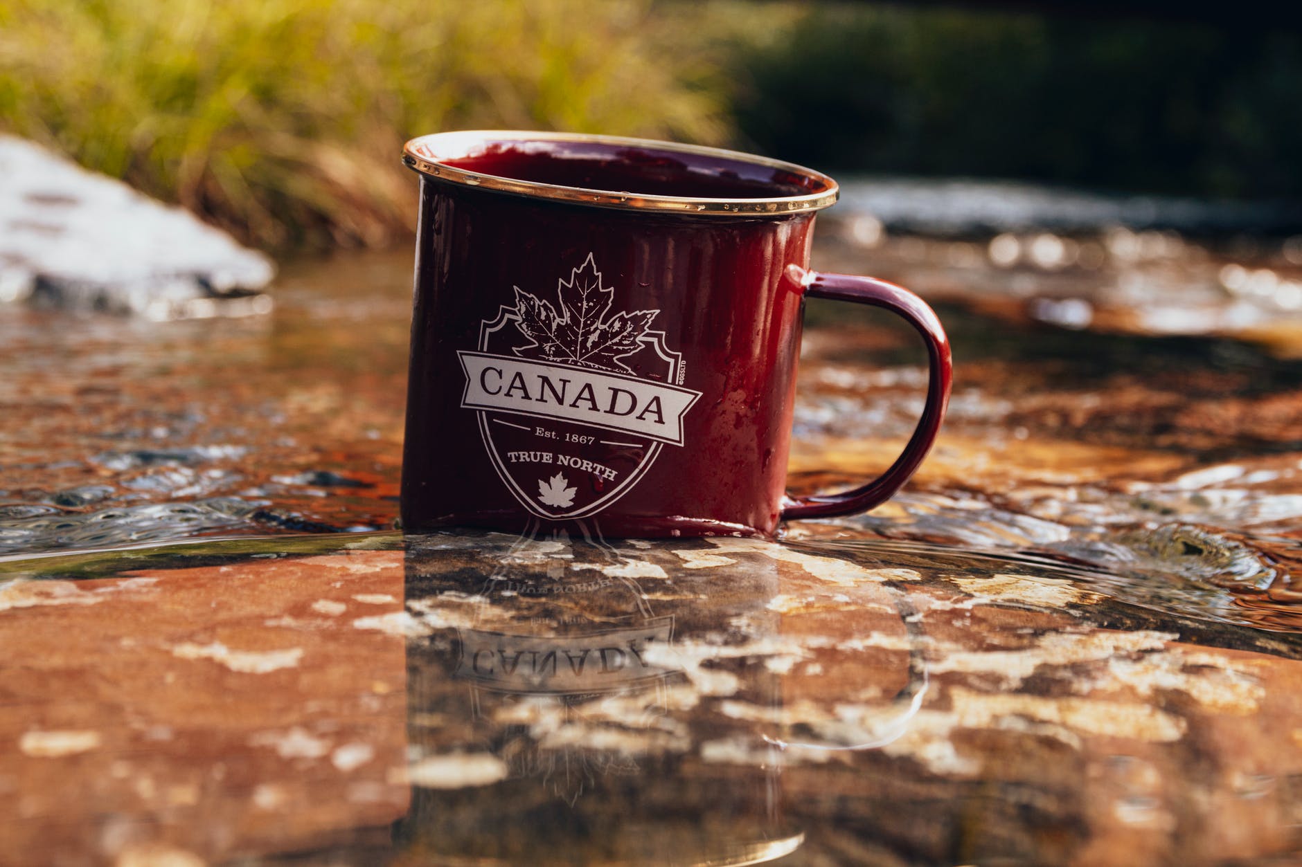 Maroon mug with Canada emblem on rock in river.