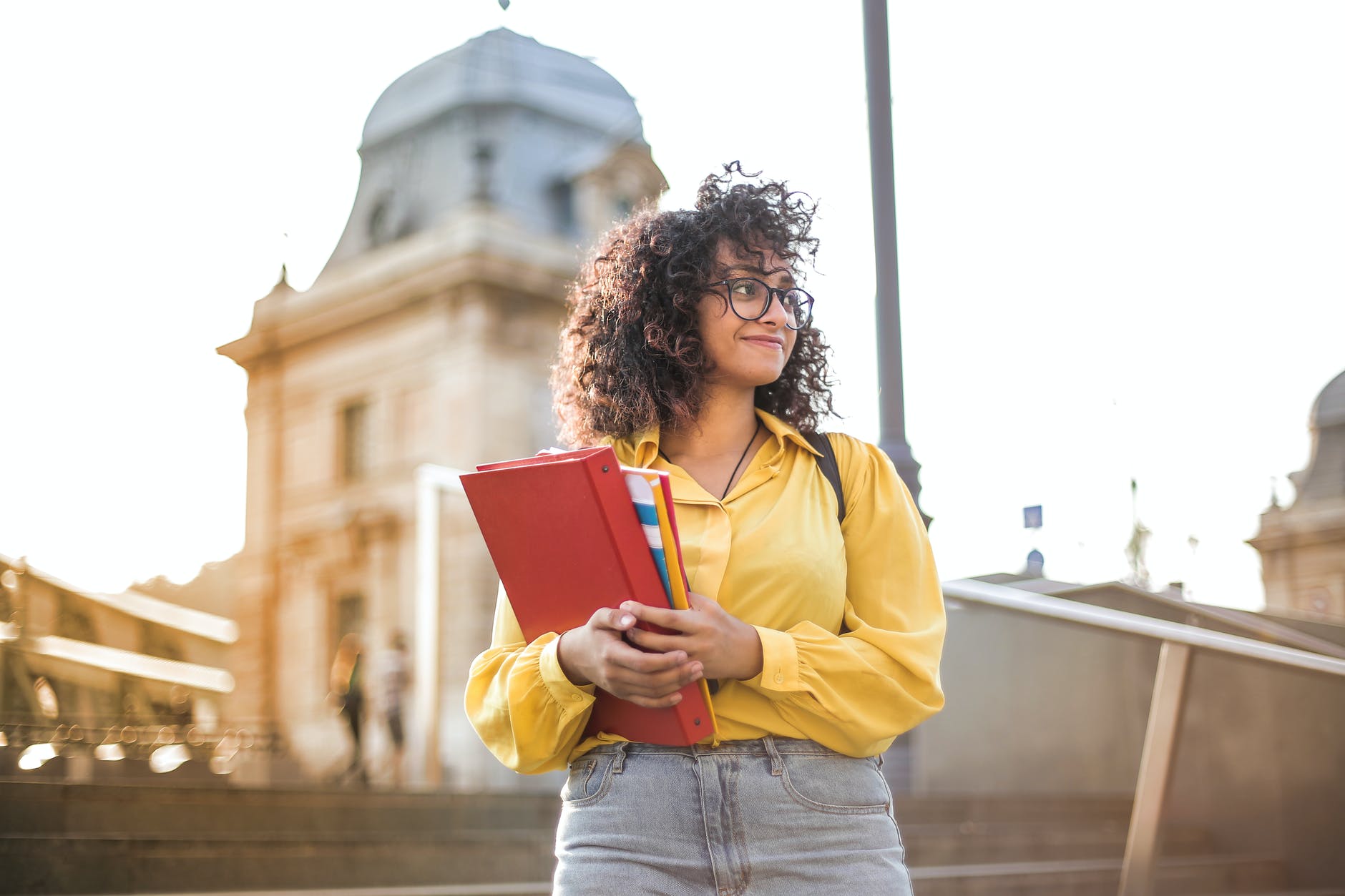 Woman with curly hair and yellow blouse holding binder and books.