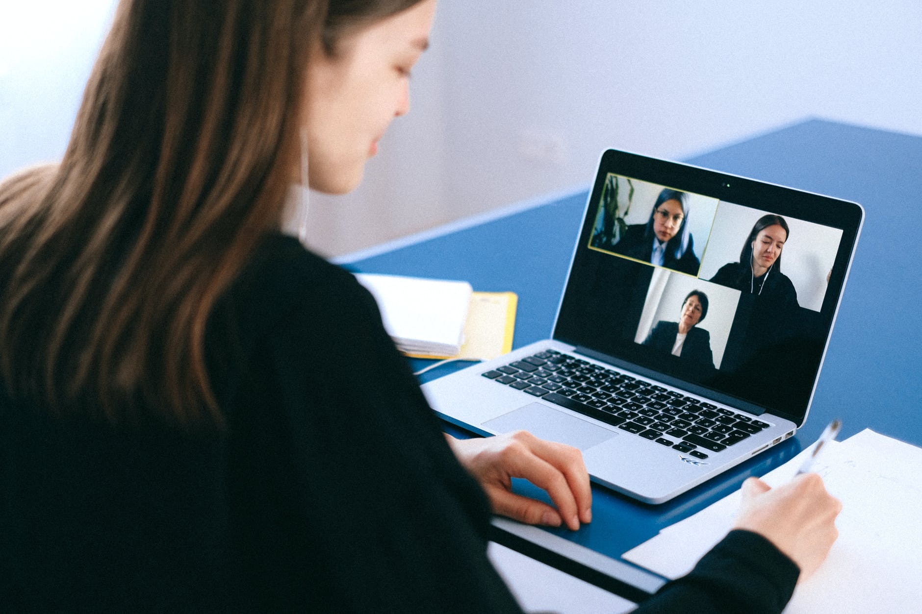 Woman working on laptop with three video boxes on screen.