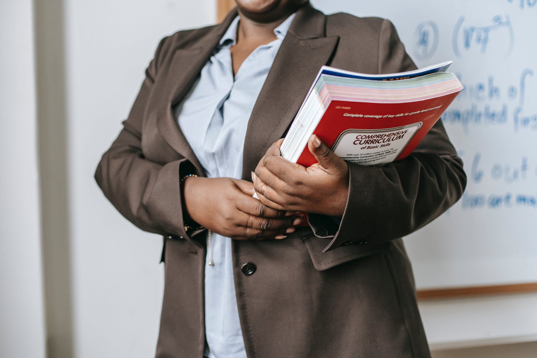 Black woman holding thick book with title "Comprehensive Curriculum."