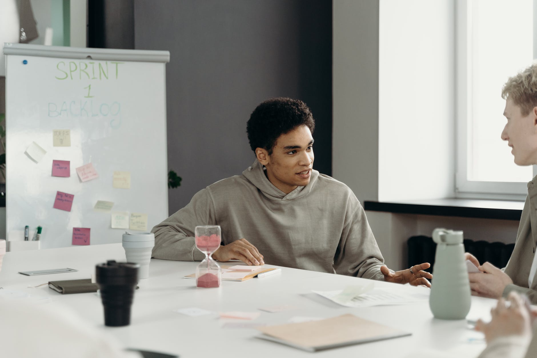 Black man at table speaking to other white man. Whiteboard in the background.