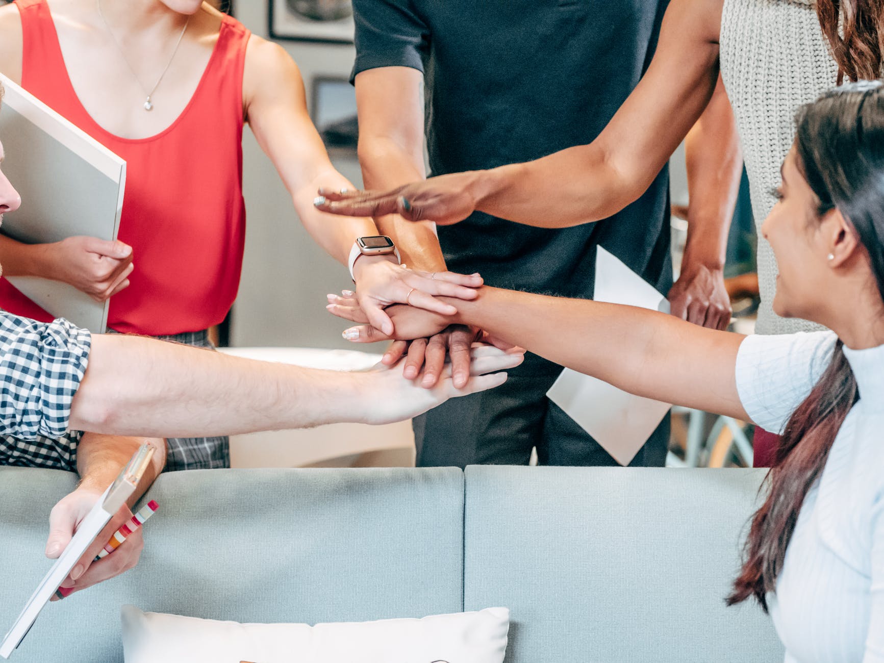 At least five sets of hands coming together over table.
