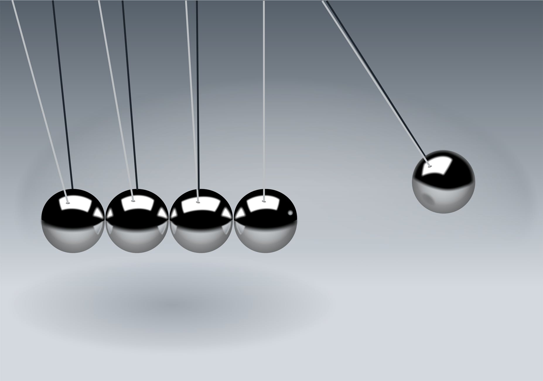 Five silver balls hanging from strings. One is separated from the other four and will swing to hit them.