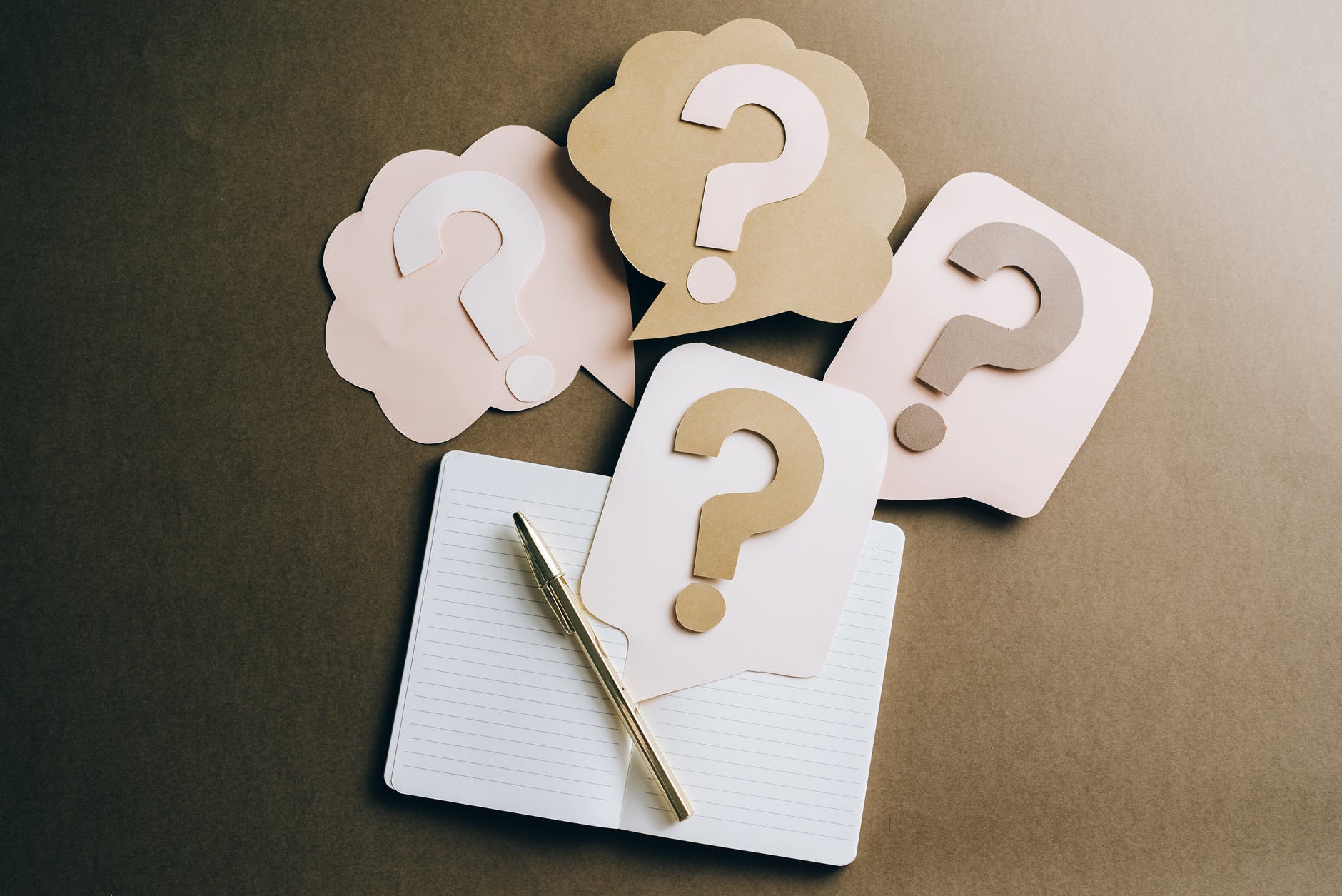 Beige paper questions marks next to notepad and gold pen.