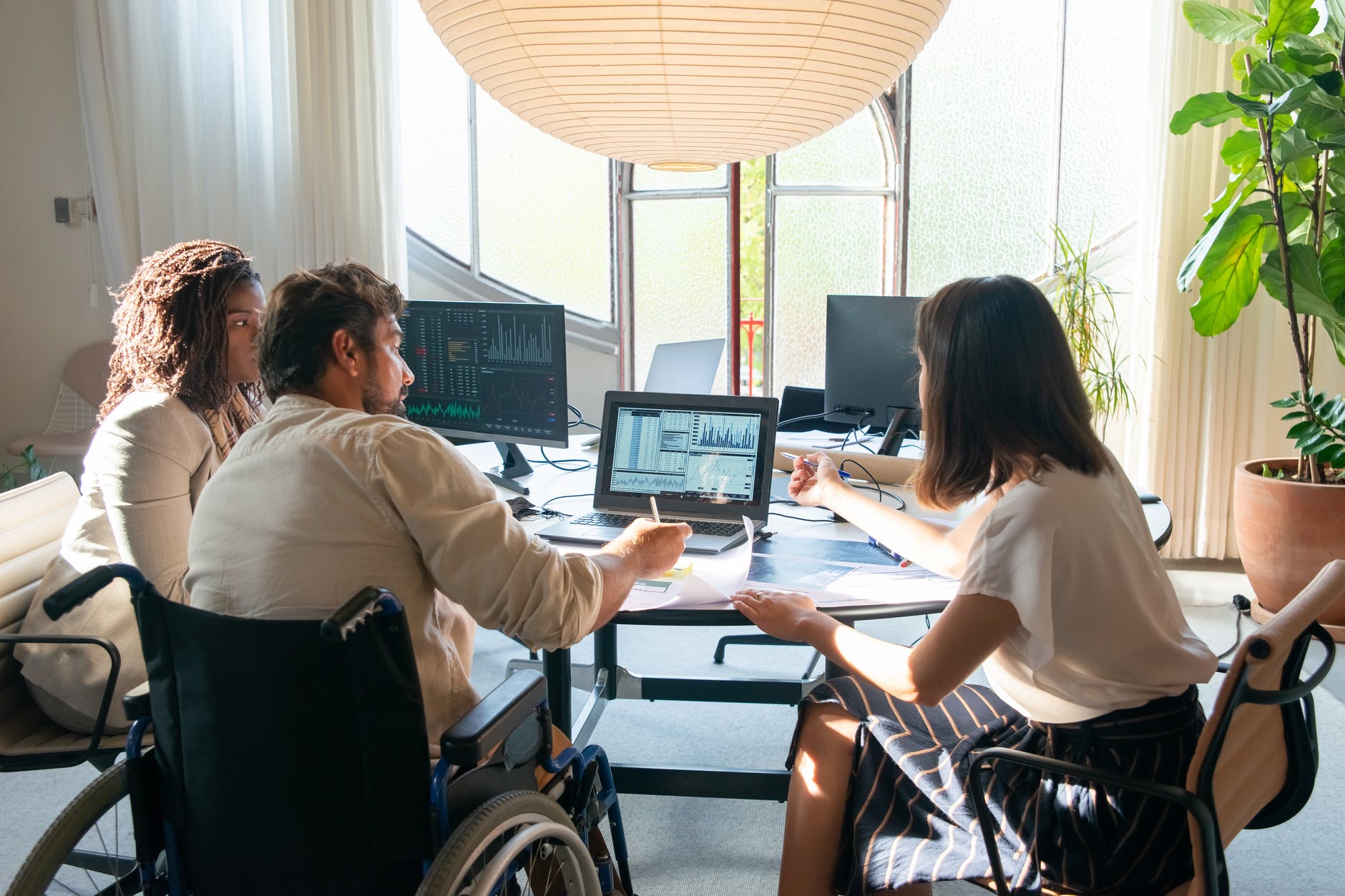 Three people at table with computers. Black woman, man with beard, back of woman with shoulder-length hair.