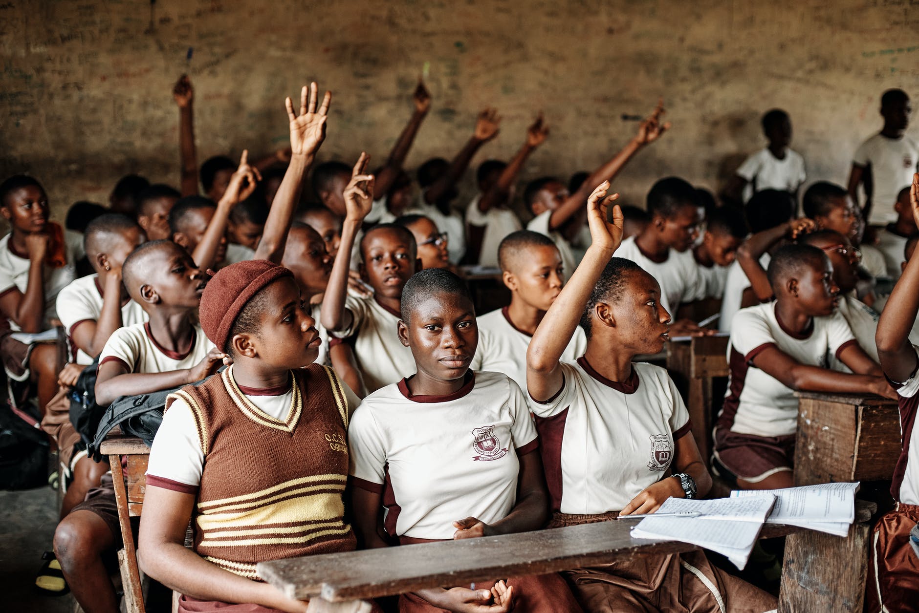 Students in classroom close together raising arms for questions.