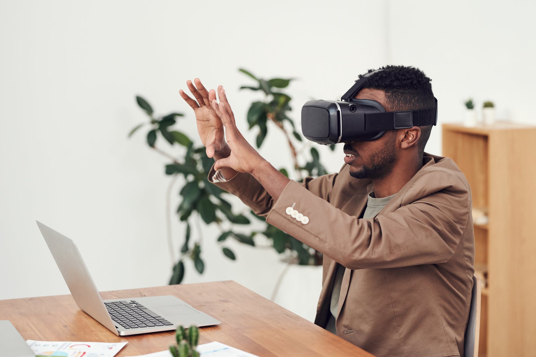 Black man in front of laptop on desk and wearing virtual reality headset