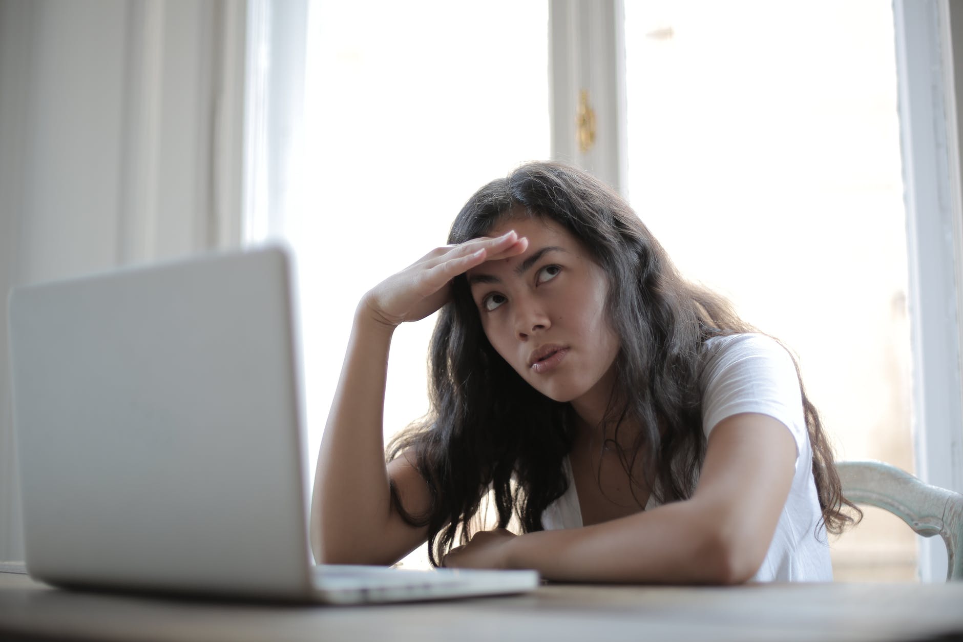Fatigued woman in front of laptop. Head is propped up by hand.