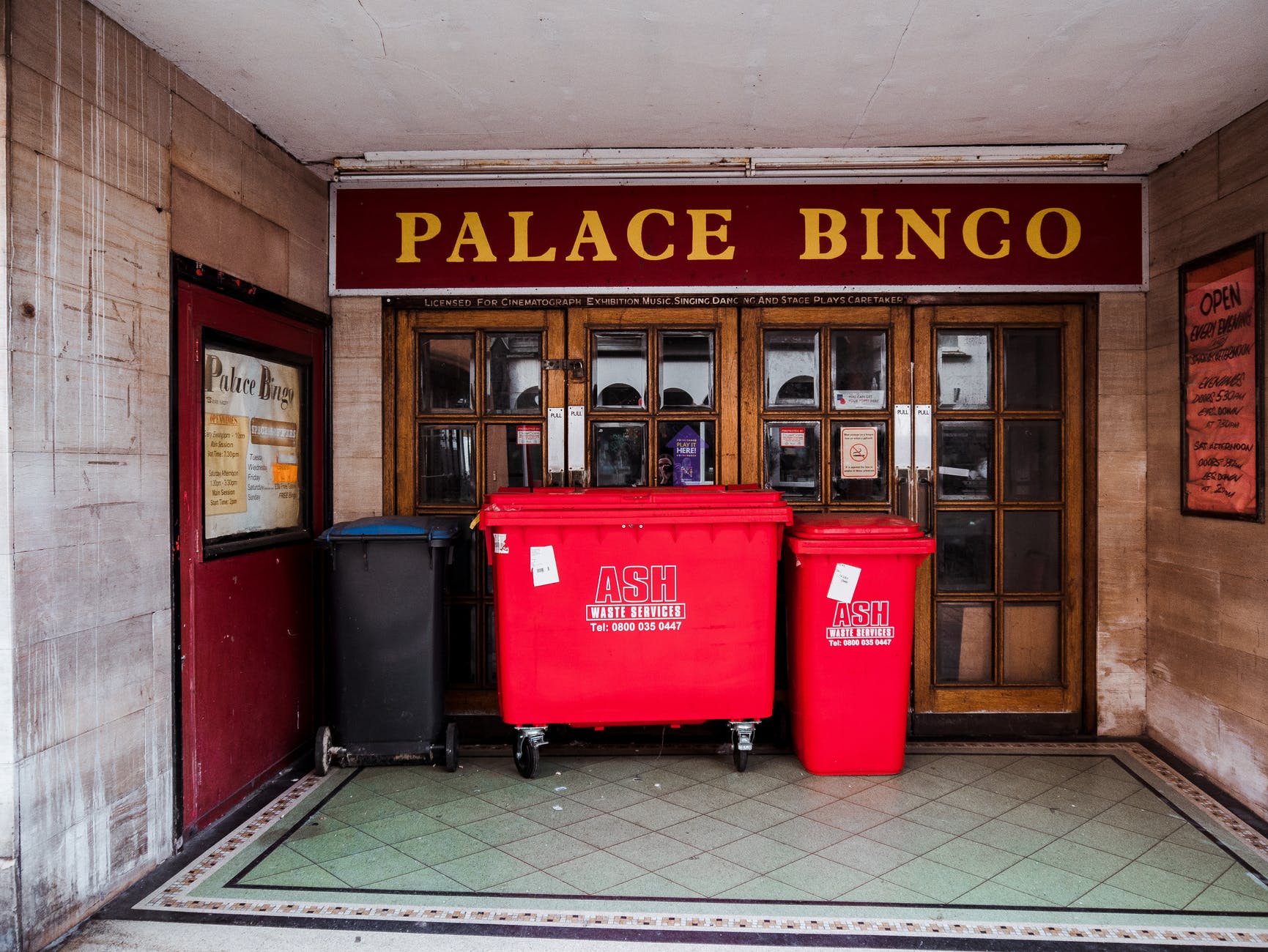 Door with sign "PALACE BINGO" and two red trashcans with white lettering "Ash Waste Services"
