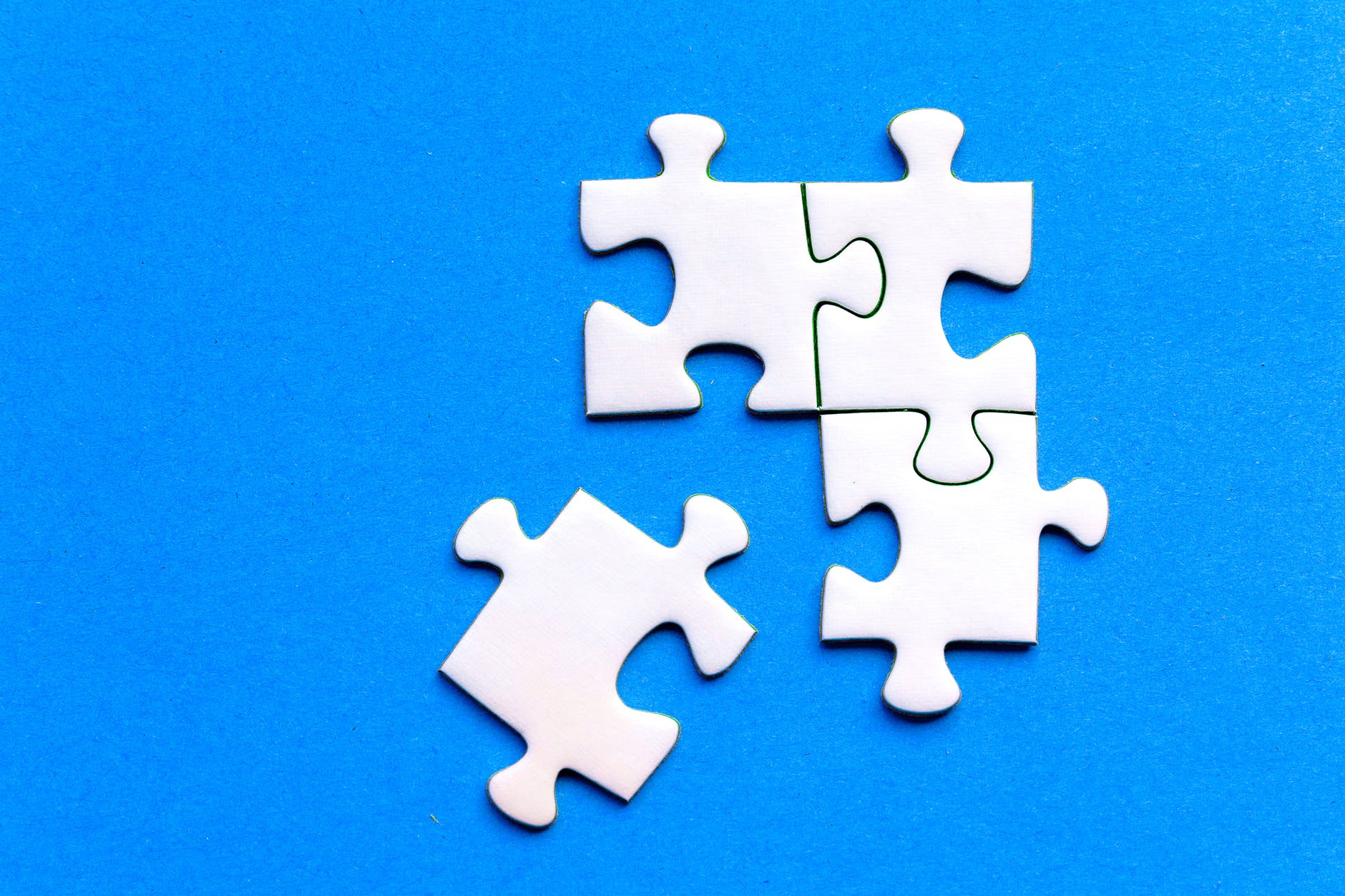 White jigsaw puzzle on blue background. Four pieces are shown with three connected to each other and one in the lower left.