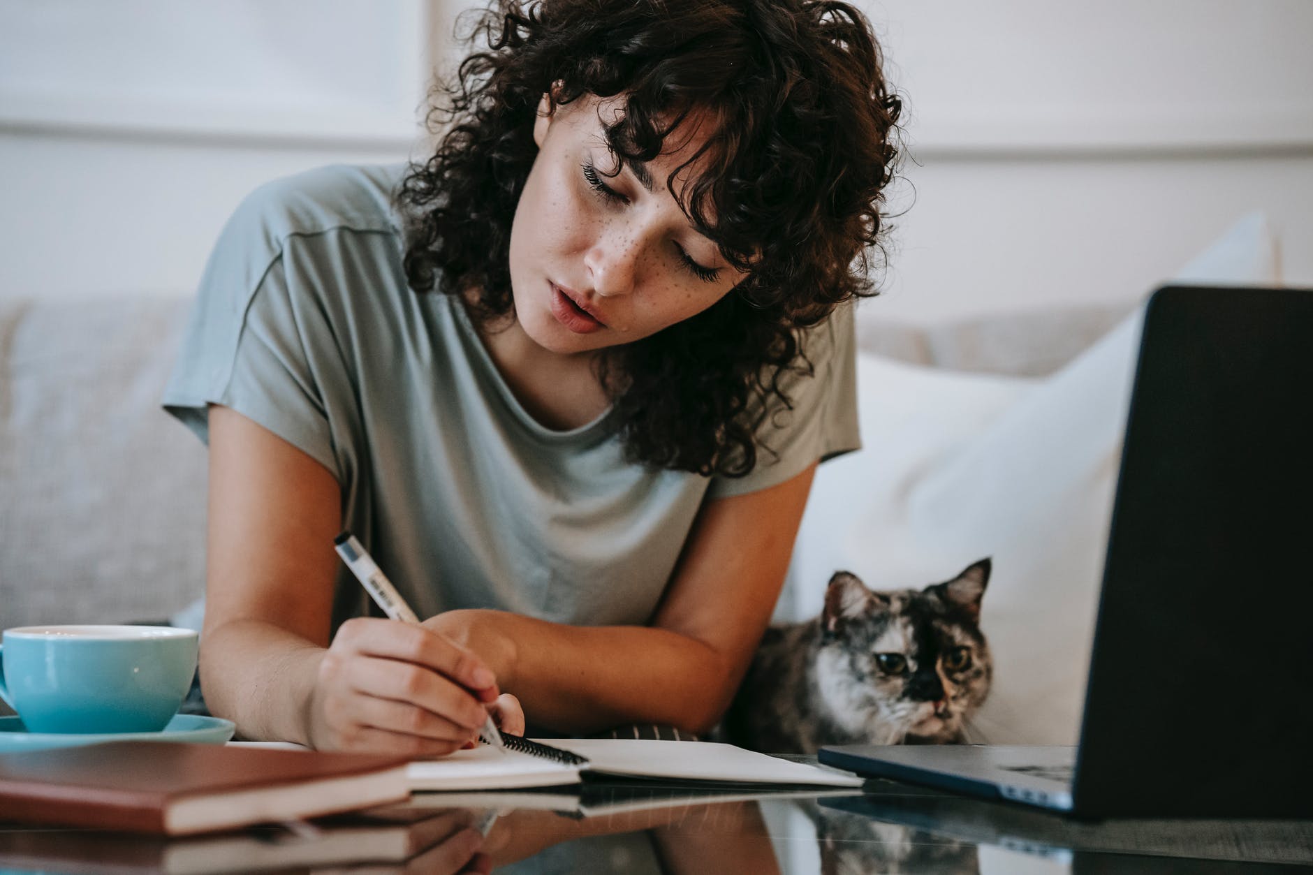 Woman with curly black hair writing with open laptop