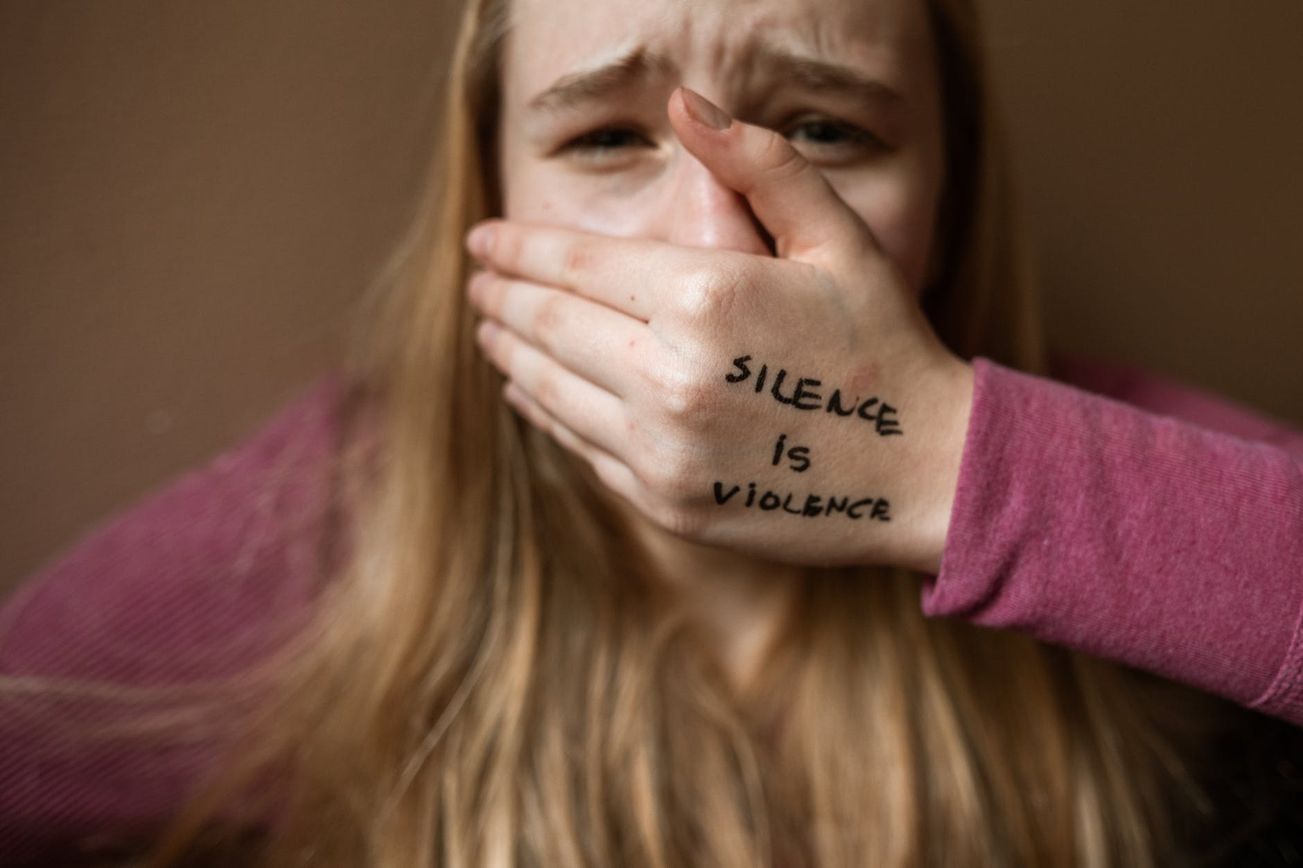 Woman covering mouth with hand. Hand has "silence is violence" written in black.
