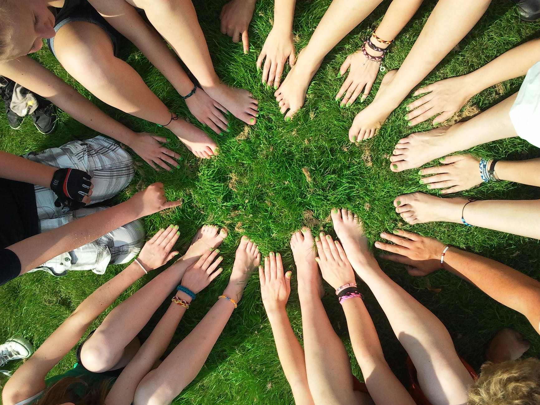 Numerous hands and feet with different skin tones on grass all forming.a circle.