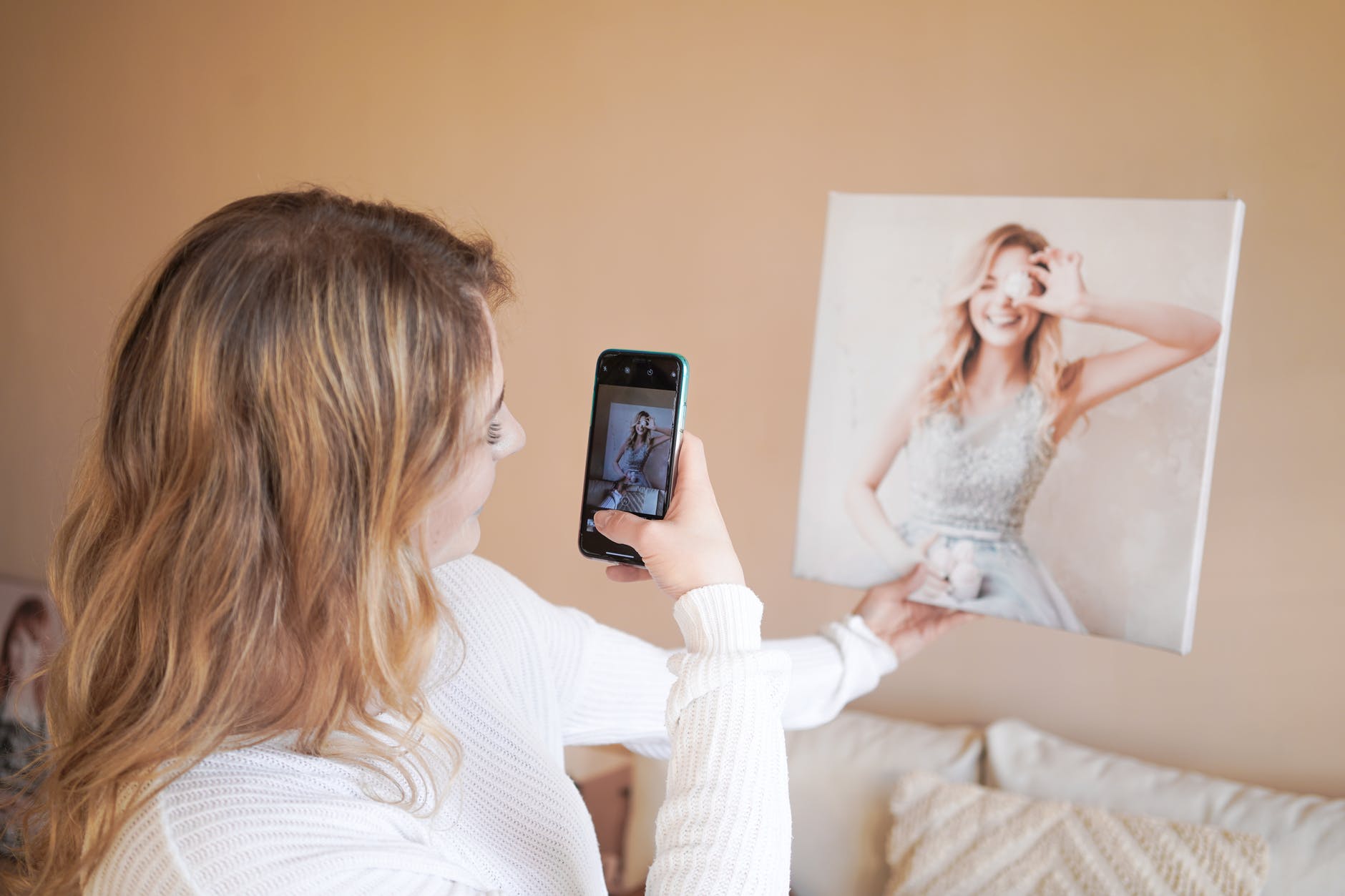 Woman taking photo with cell phone of square painting of blond woman