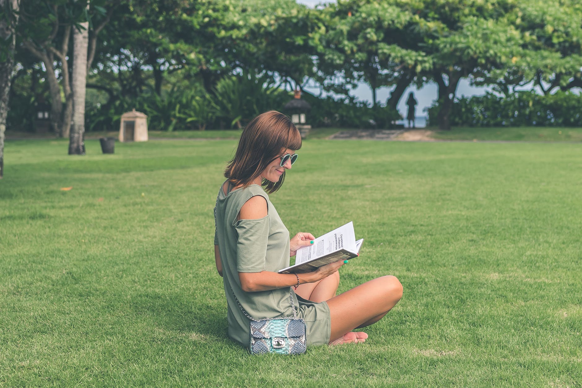 female student reading book on grass