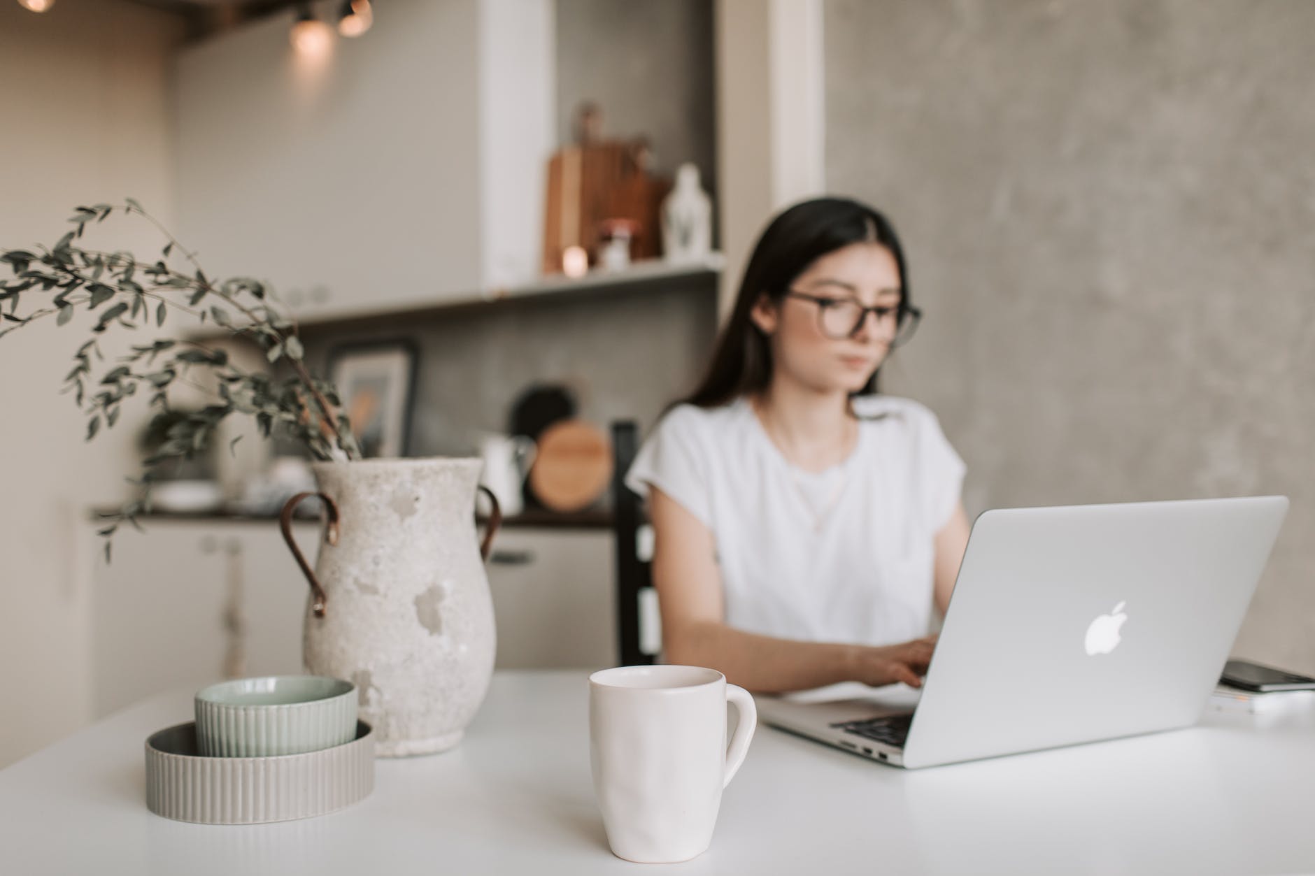 Woman working on laptop at table with vase and white mug