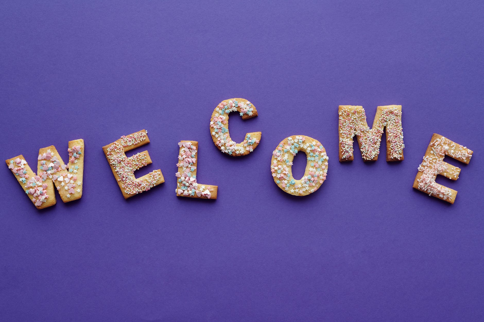 purple background with cookies in the shape of letters spelling:
W E L C O M E