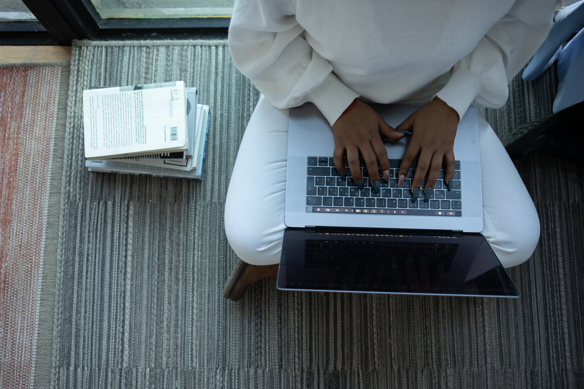 top down view of laptop and two hands on keyboard and stack of books
