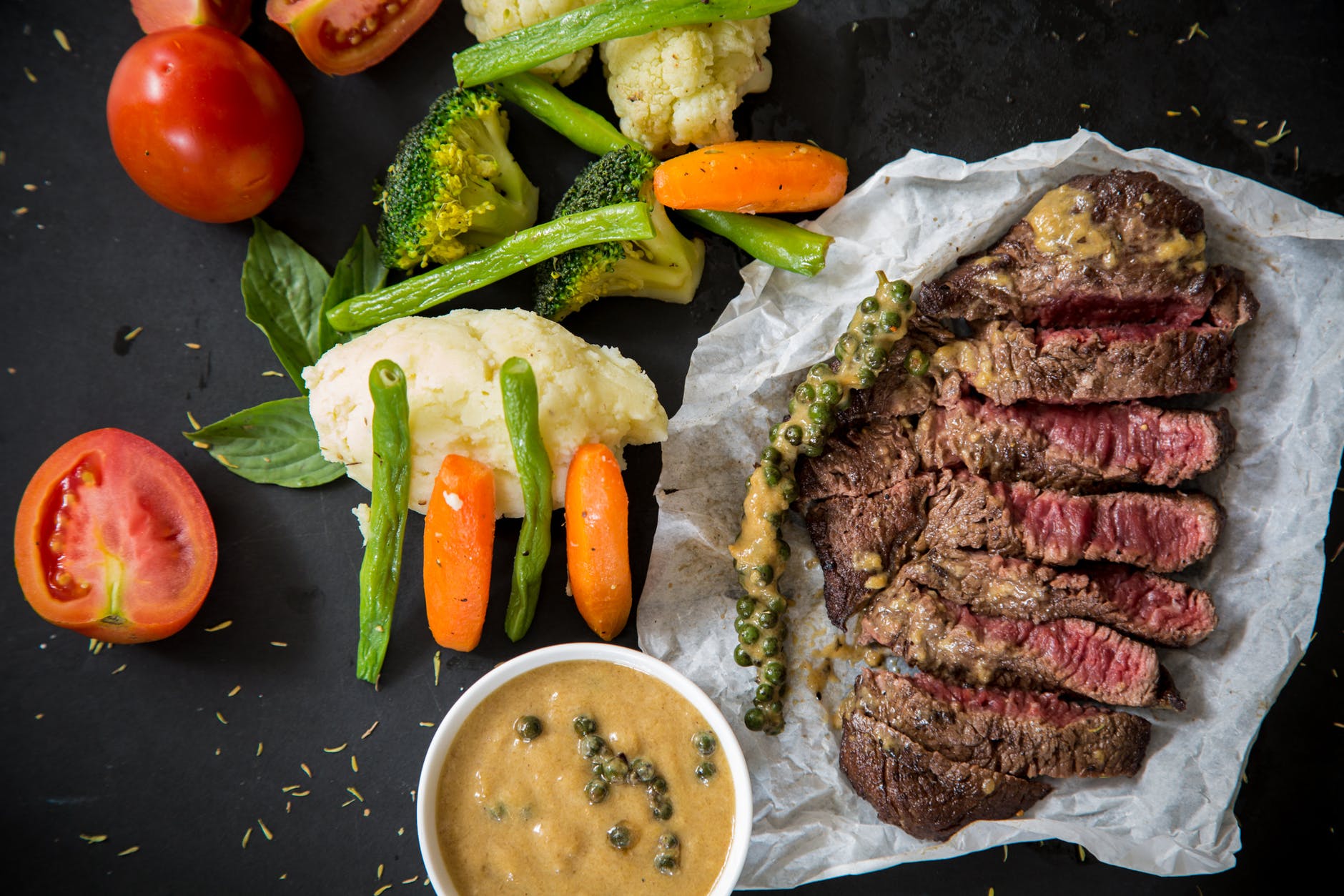 Meat meal and vegetables on table. Gravy is in cup.