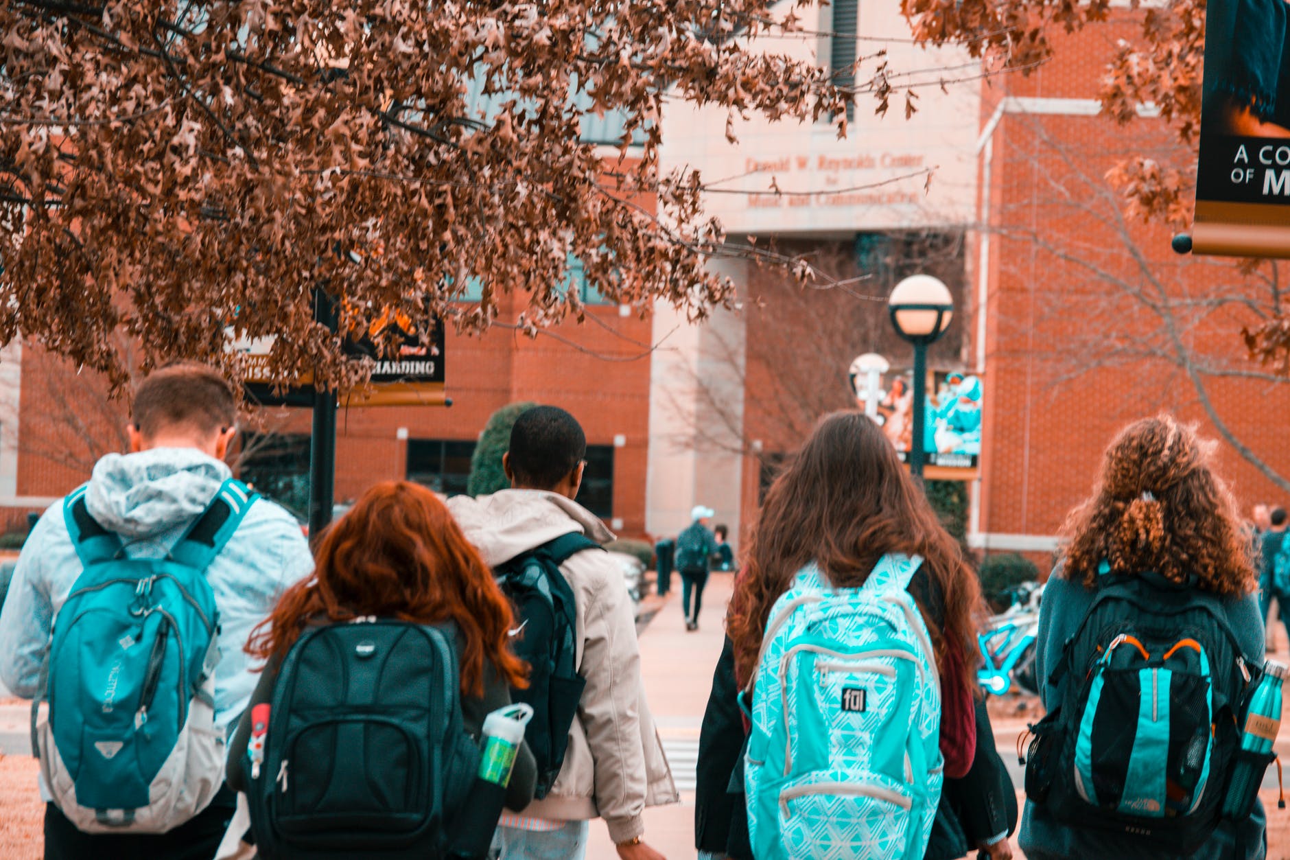 backs of students with backpacks heading to building