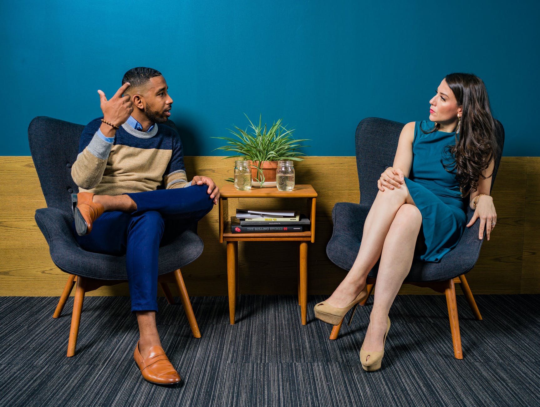Black man with short hair and white woman with brown hair seated in blue chairs talking