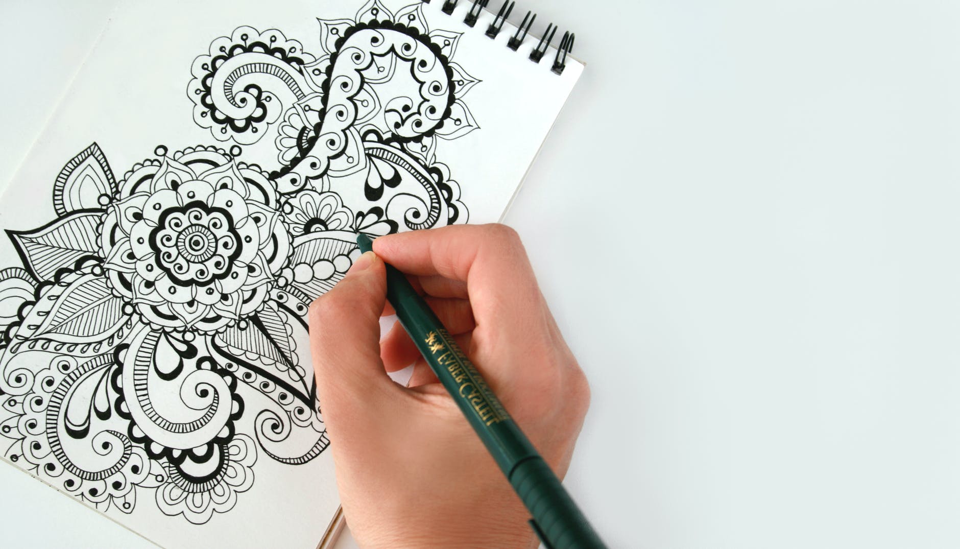 top down view of notebook, hand holding pencil, and intricate pattern