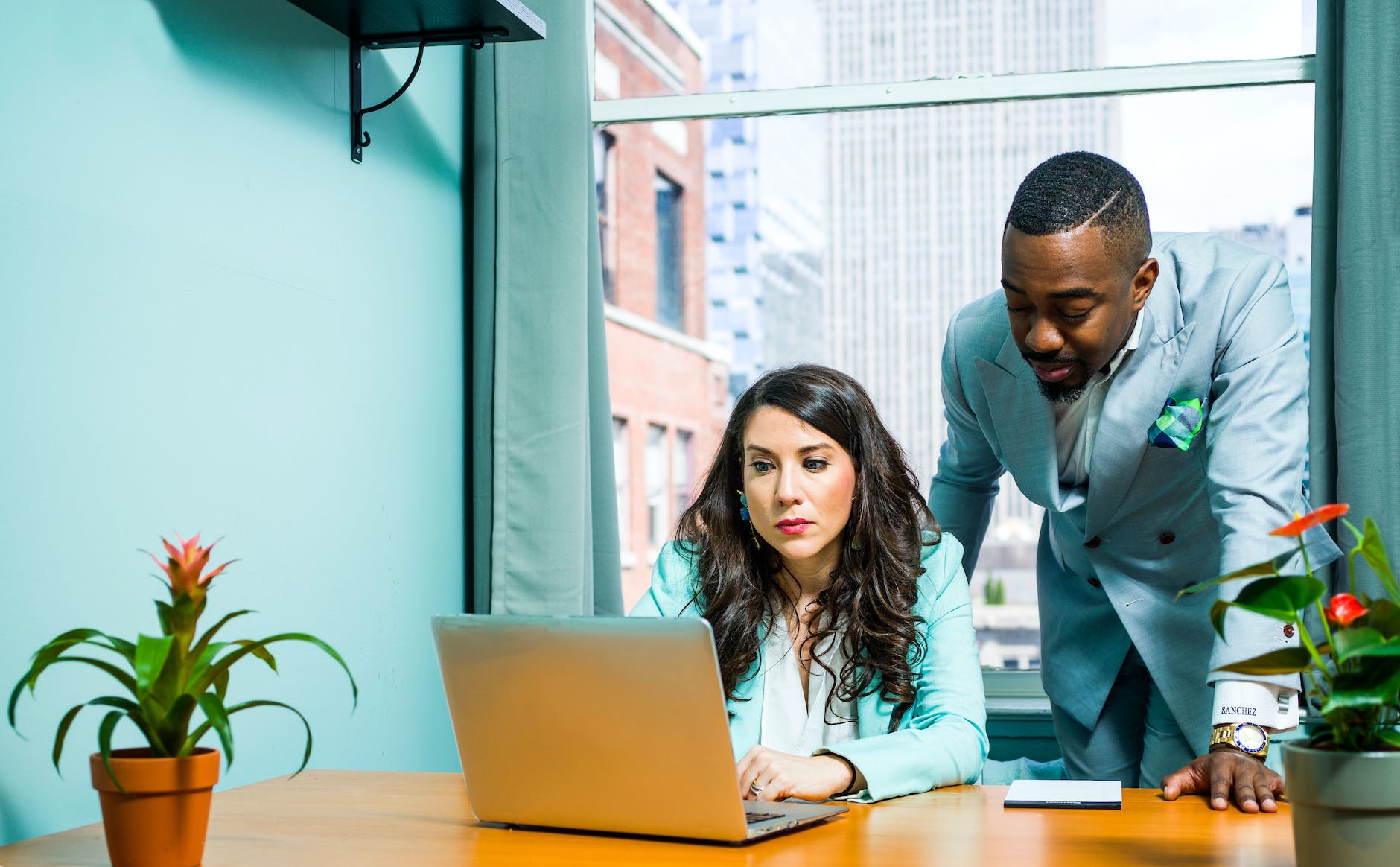 woman working on laptop and man wearing suit standing next to them
