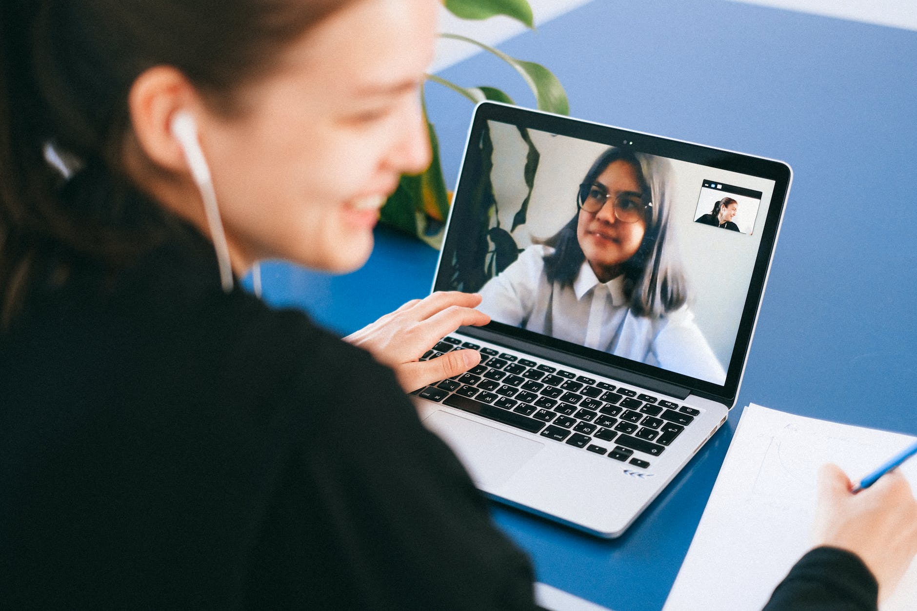 One woman on the screen of a laptop and another with headphones engaging in a videoconference.
