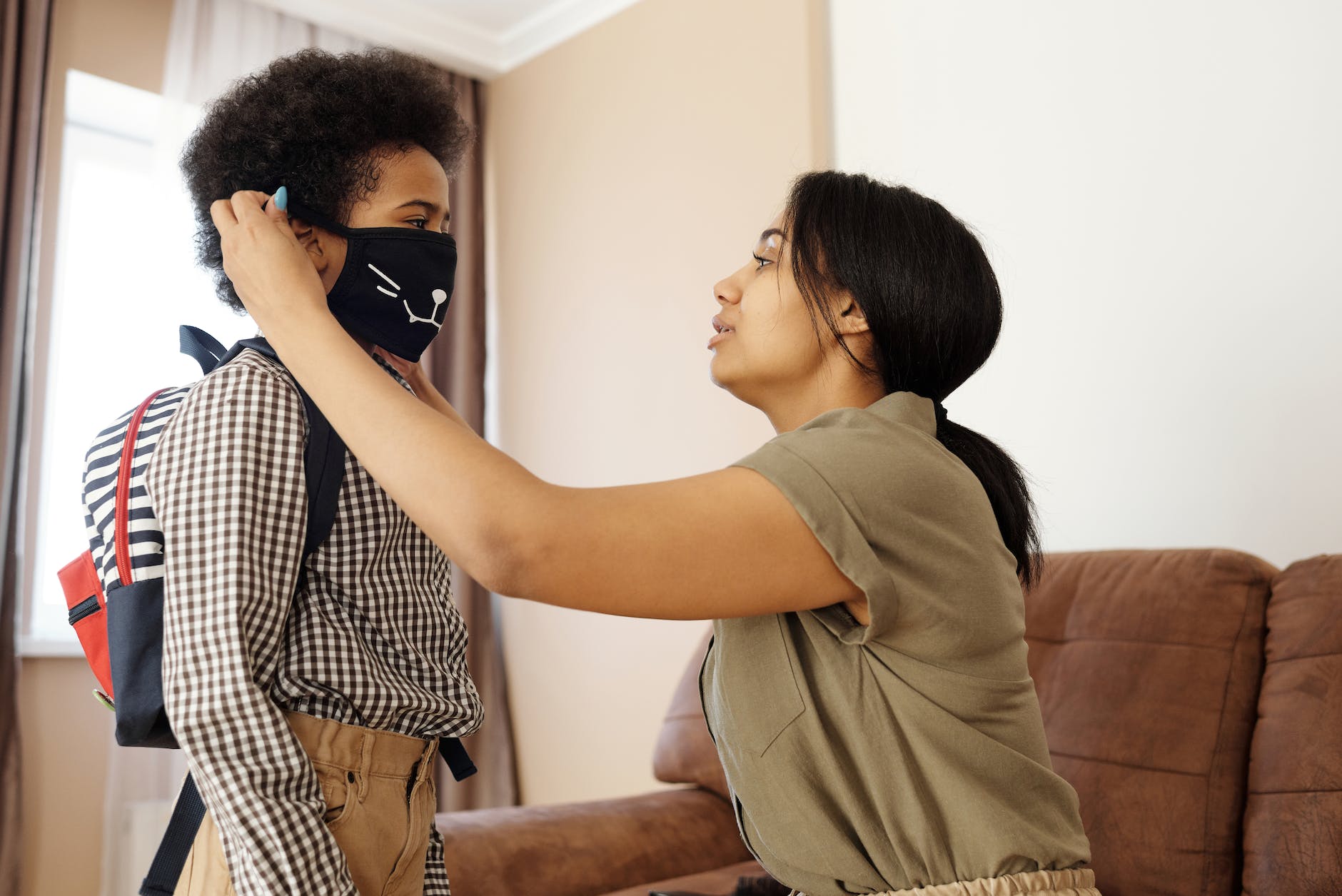 Black woman kneeling and putting mask on young black boy with backpack