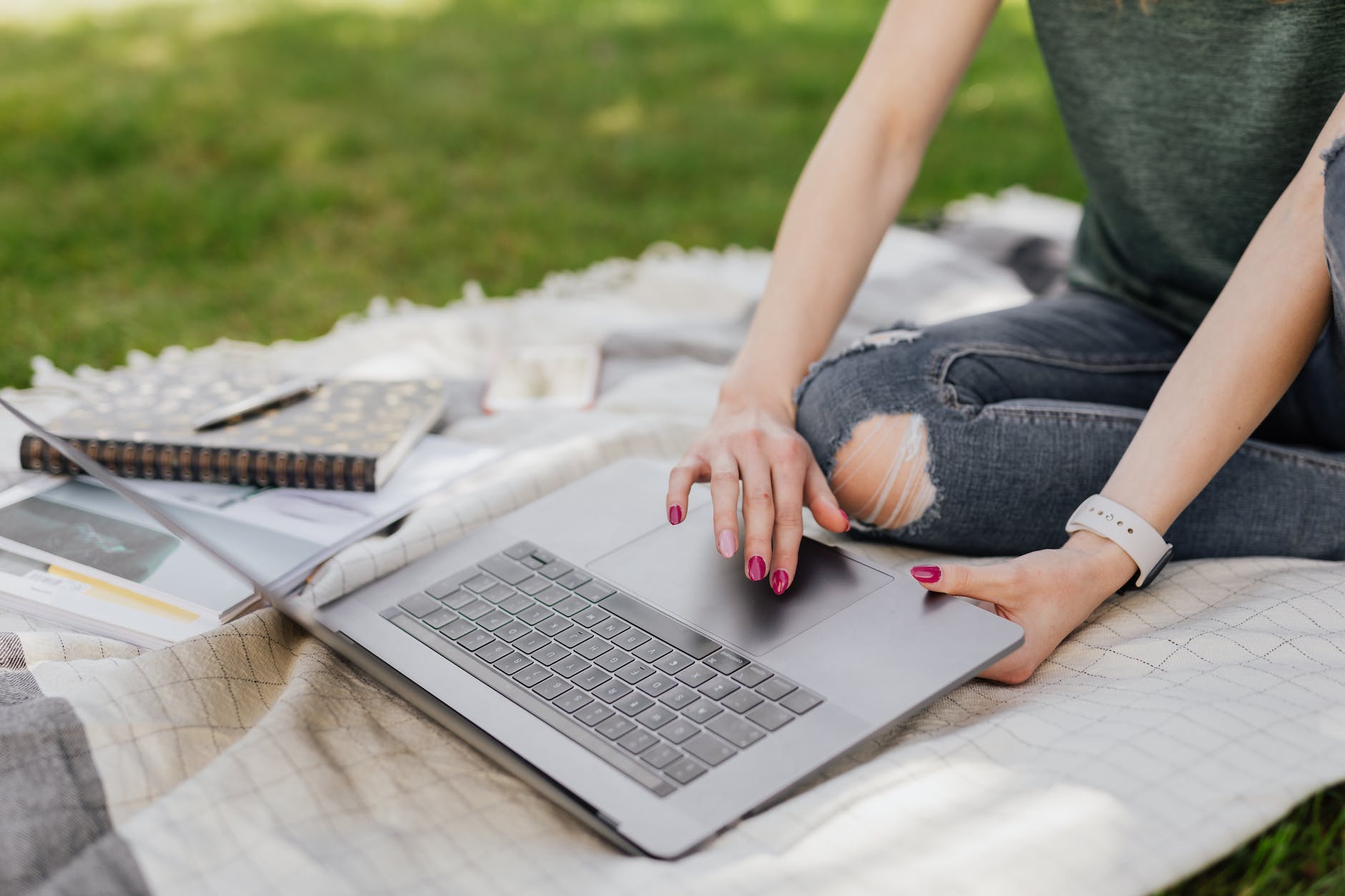 person sitting on blanked outside in grass with open laptop