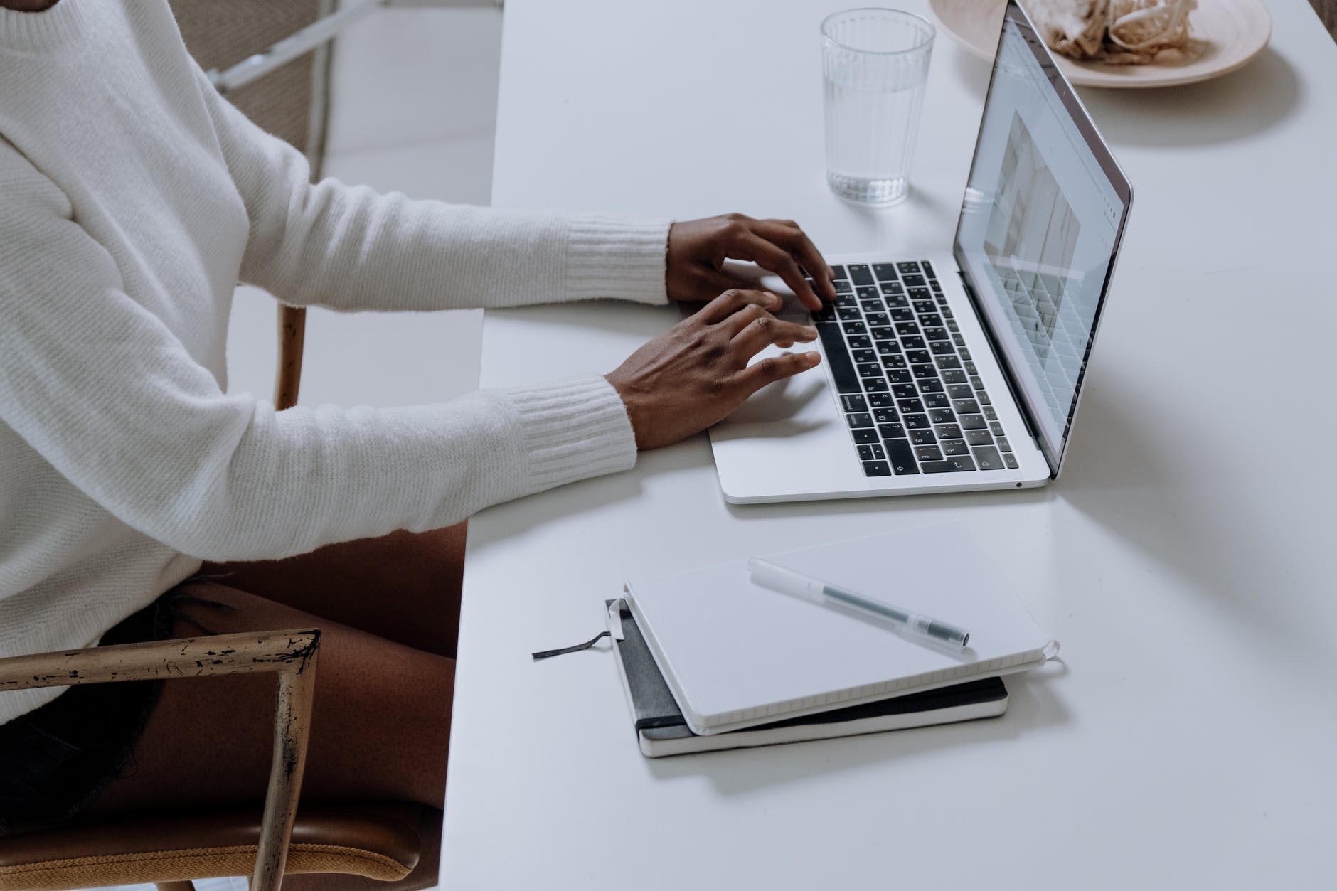 open laptop on whited esk with person with dark skin wearing white sweater typing