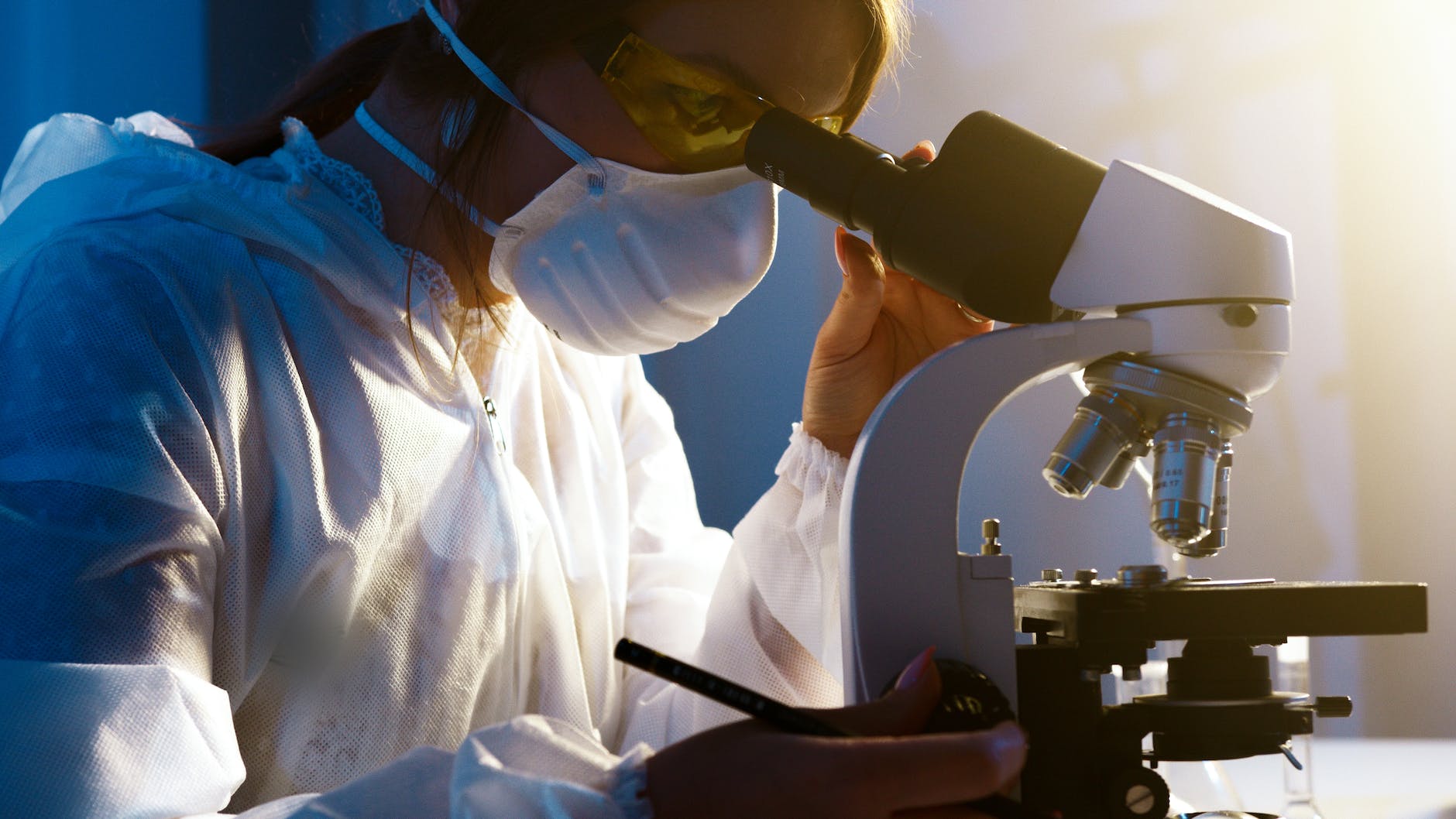 Woman wearing mask and eye protection working with microscope